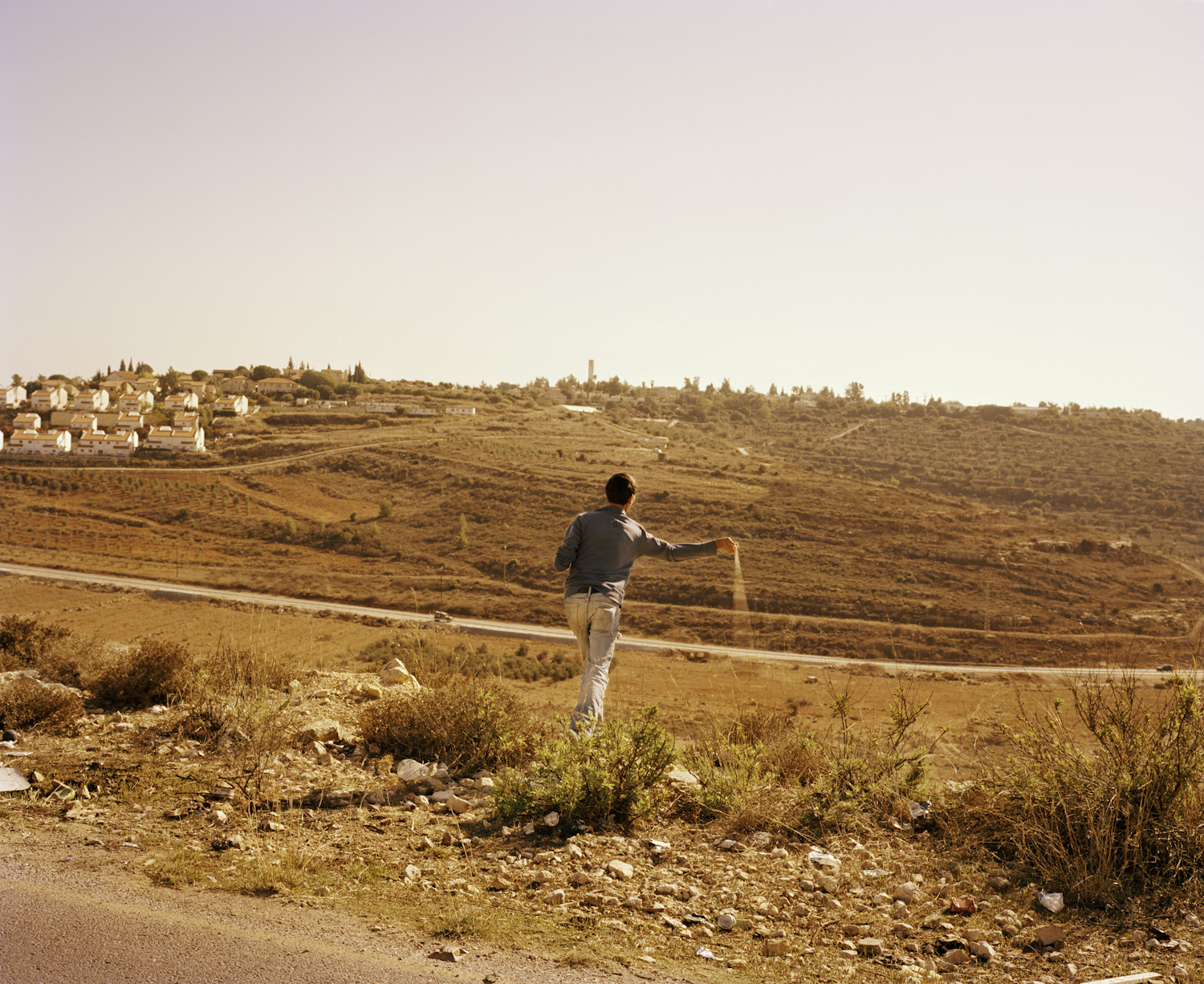 <b>Thrower (Nabi Saleh)</b><br>A Palestinian teenager in the West Bank village of Nabi Saleh uses a sling to hurl stones at Israeli soldiers amassing at the bottom of the hill. Every Friday local residents, Israeli activists and international activists gather in the village to stage non-violent demonstrations denouncing the Israeli Occupation and asserting Palestinian human rights. The protesters are met each week with tear gas and other aggressive crowd dispersal tactics, transforming peaceful demonstrations into violent exchanges of stones, rubber bullets and mass arrests.