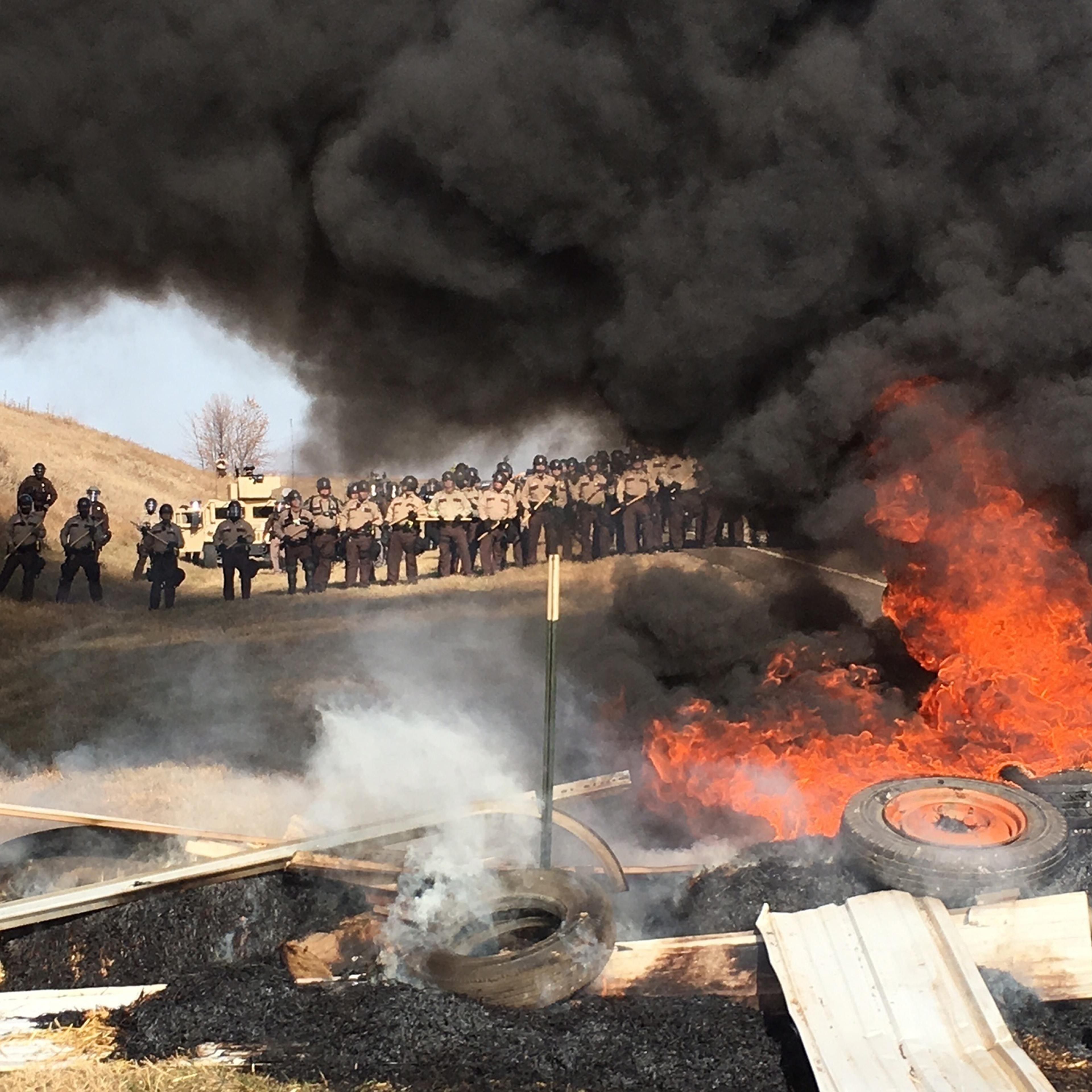 Tires burn as armed soldiers and law enforcement officers stand in formation to force Dakota Access pipeline protesters off private land in Morton County, N.D., where they had camped to block construction on Oct. 27, 2016.