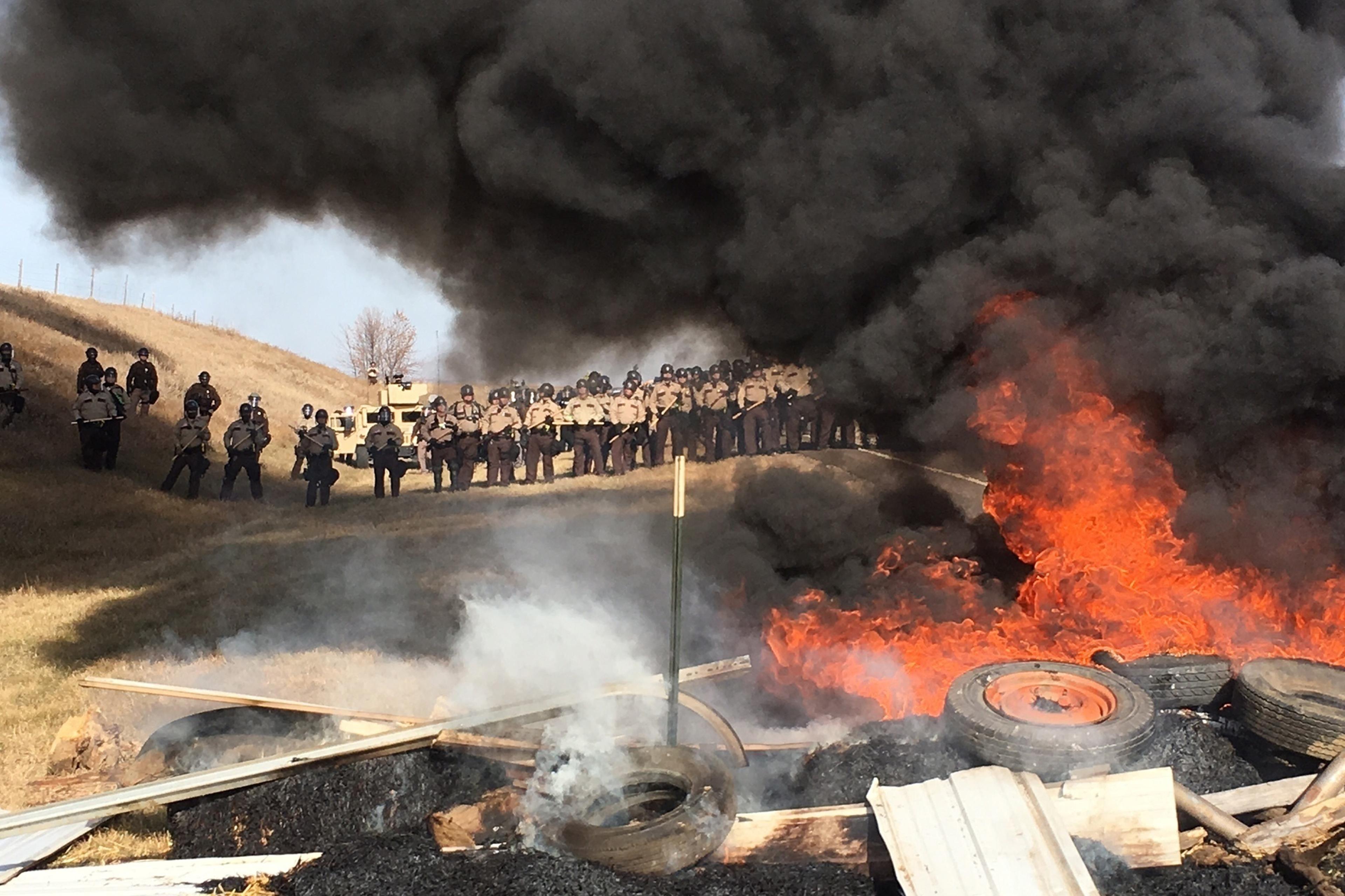 Tires burn as armed soldiers and law enforcement officers stand in formation to force Dakota Access pipeline protesters off private land in Morton County, N.D., where they had camped to block construction on Oct. 27, 2016.