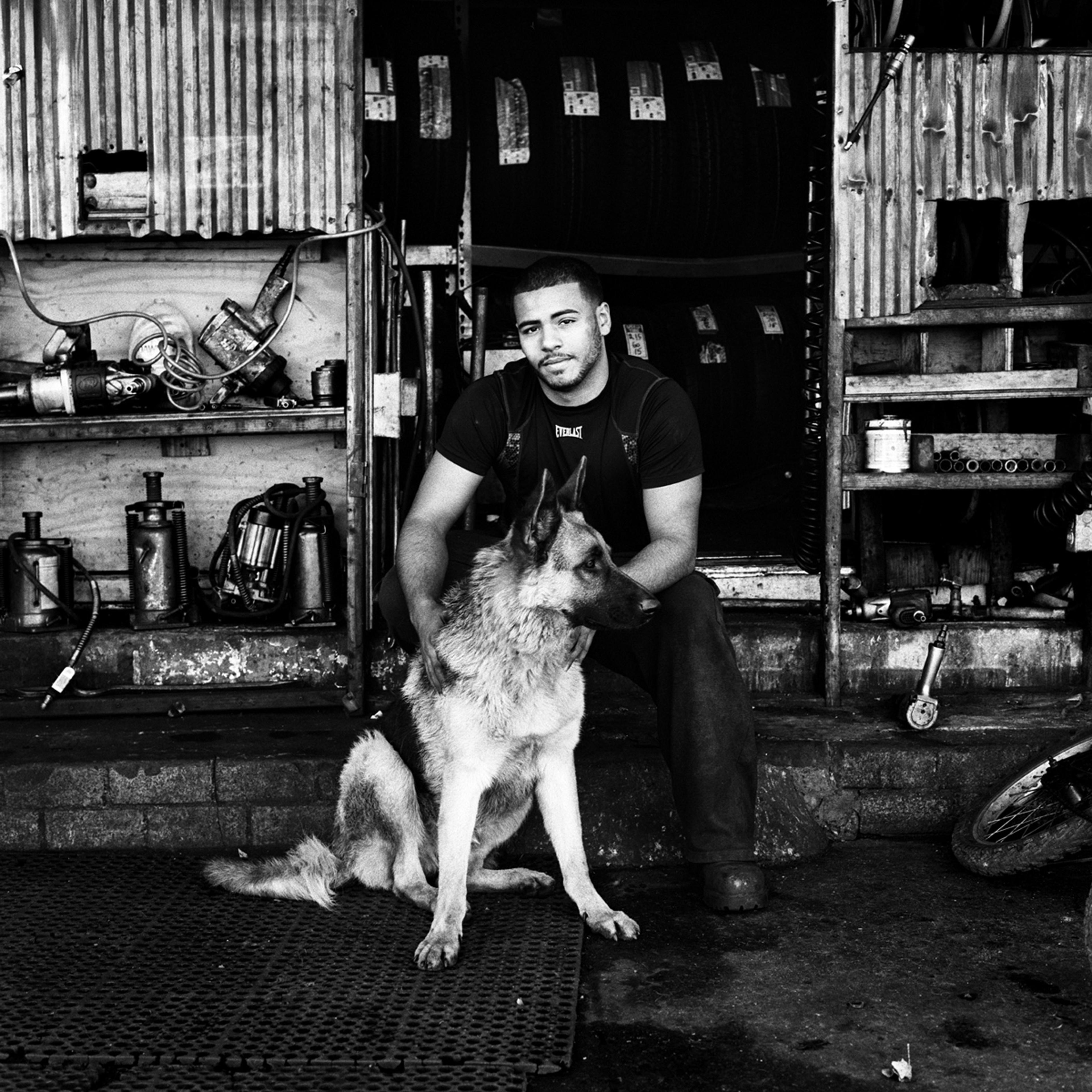 Anthony and his dog Riley at the entrance to their tire shop, P&J Tire Shop, on Metropolitan Avenue in Bushwick, Brooklyn, N.Y., November 2015.