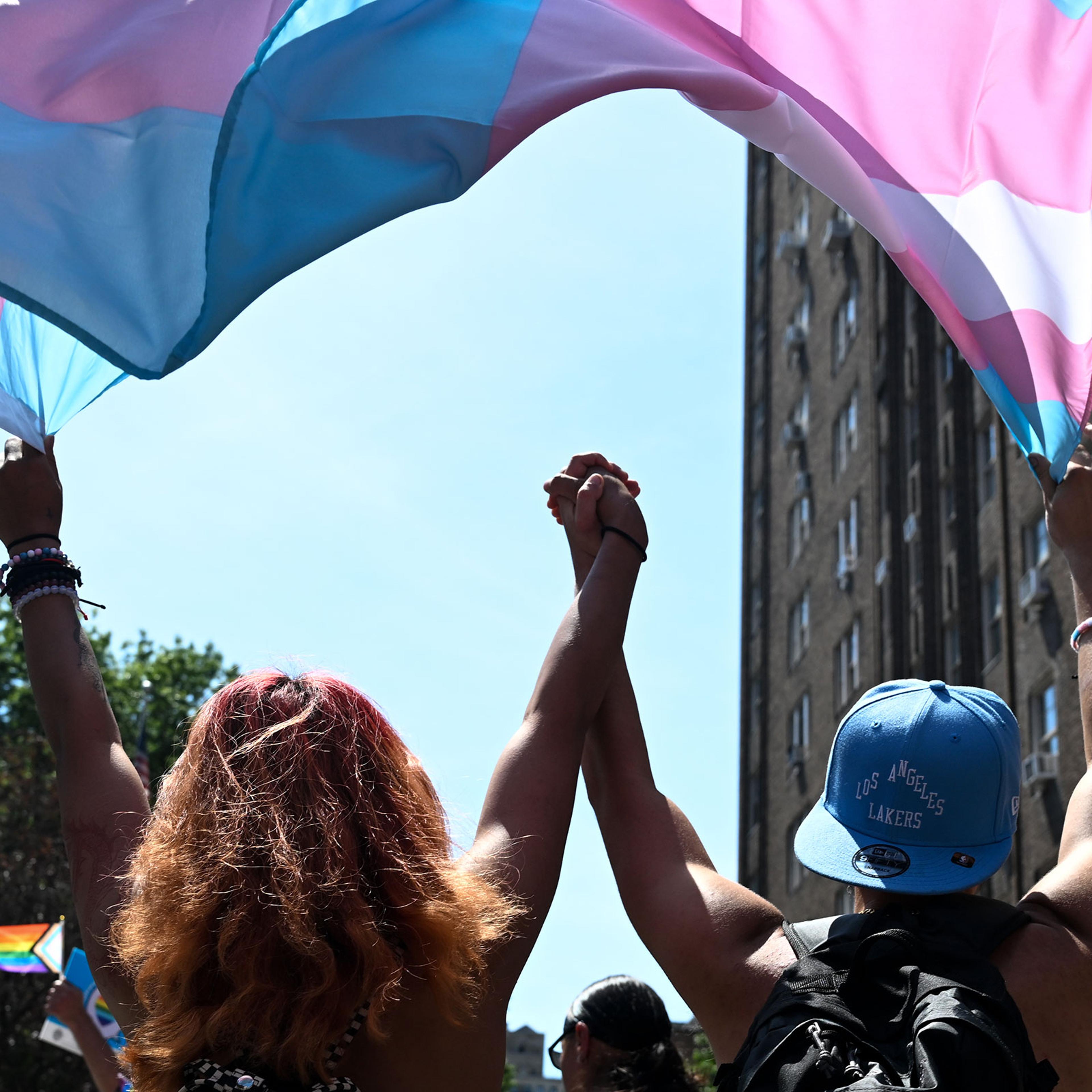 Two people hold hands while marching under a trans pride flag in the New York City Pride Parade on June 26, 2022.