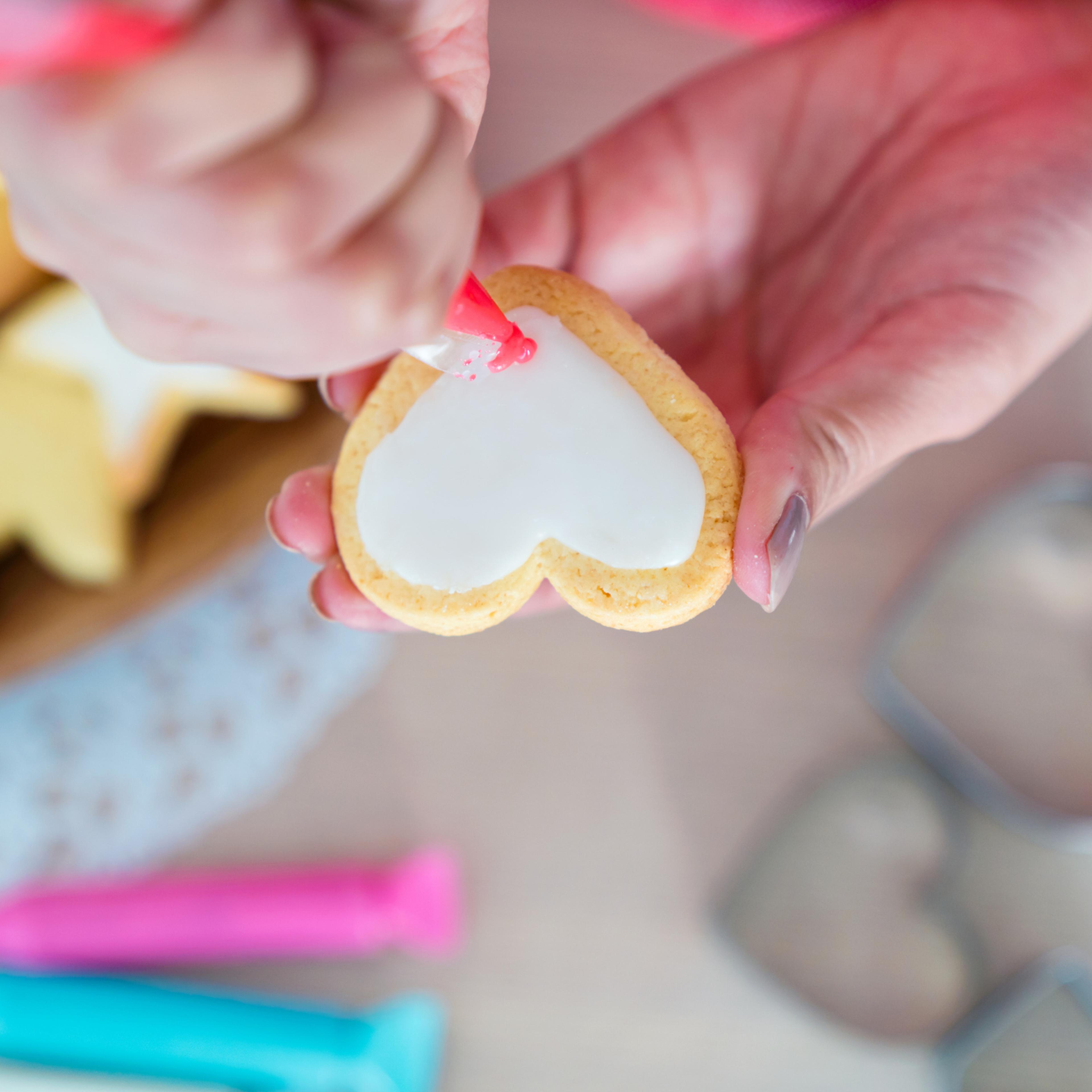 Overhead view of a woman icing a heart shaped cookie