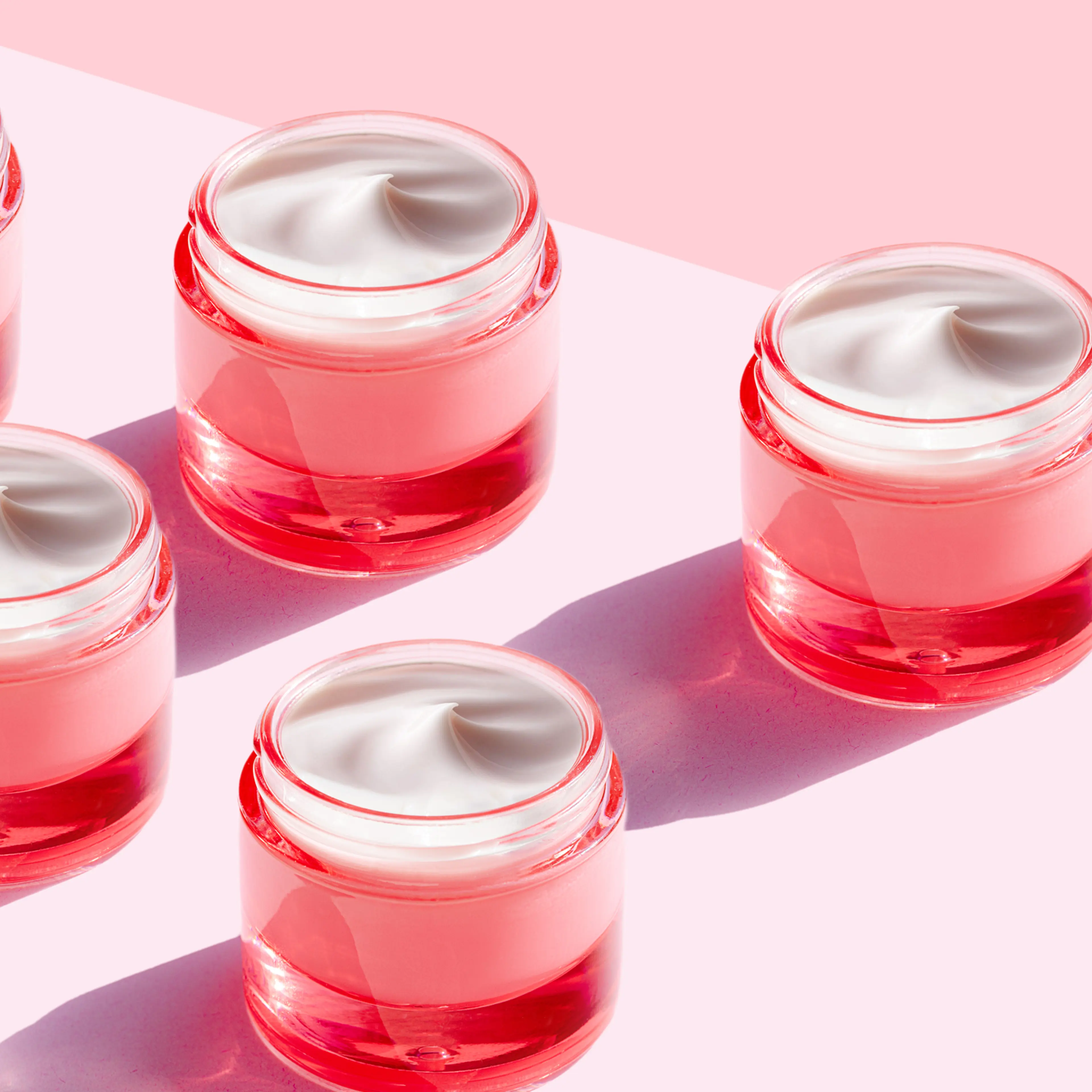 Tubs of moisturizing cream on a pink background.