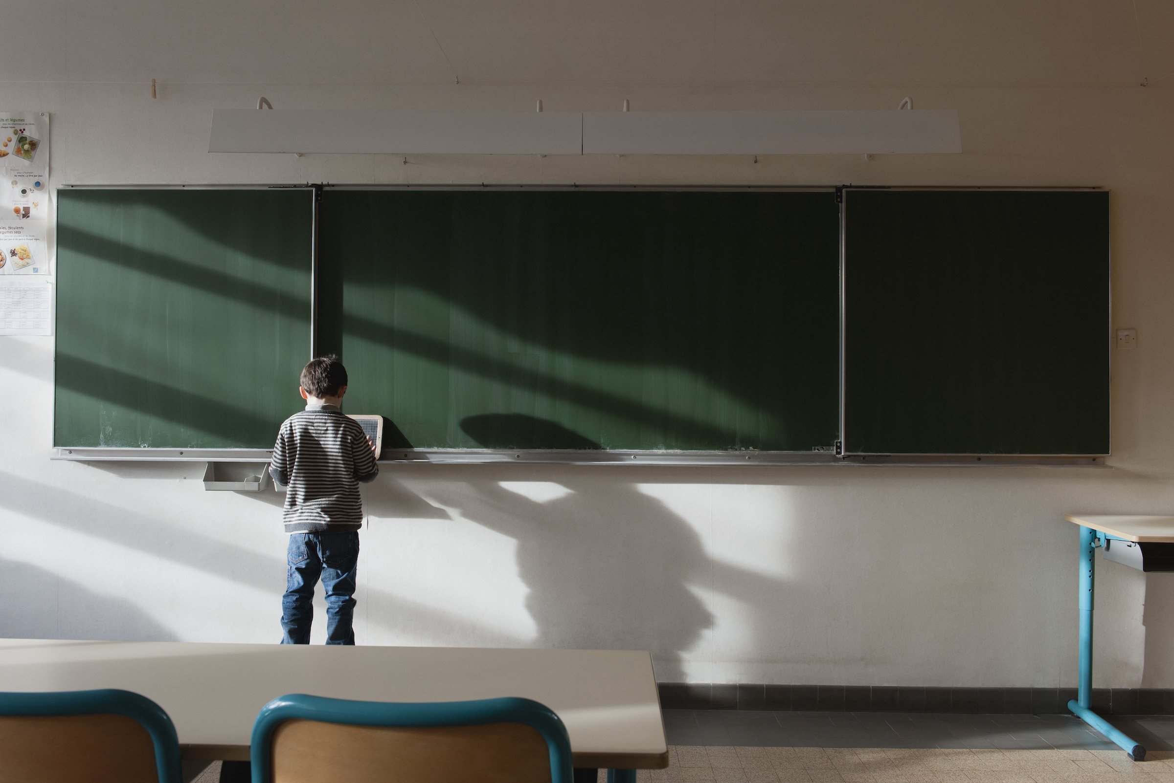 Boy standing in classroom, in front of blackboard, rear view