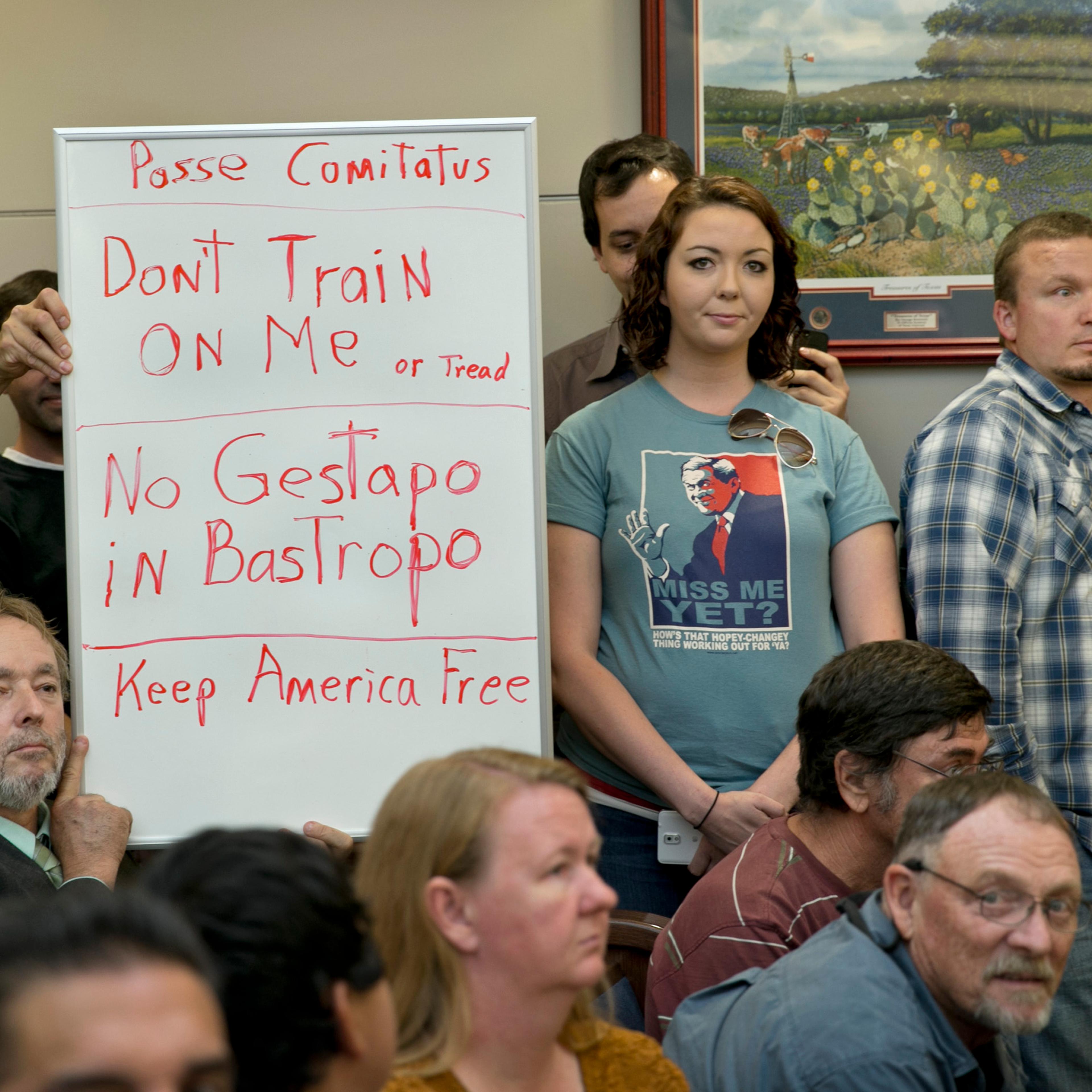 Bob Welch, standing at left, and Jim Dillon, hold a sign at a public hearing about the Jade Helm 15 military training exercise in Bastrop, Texas, April 27, 2015