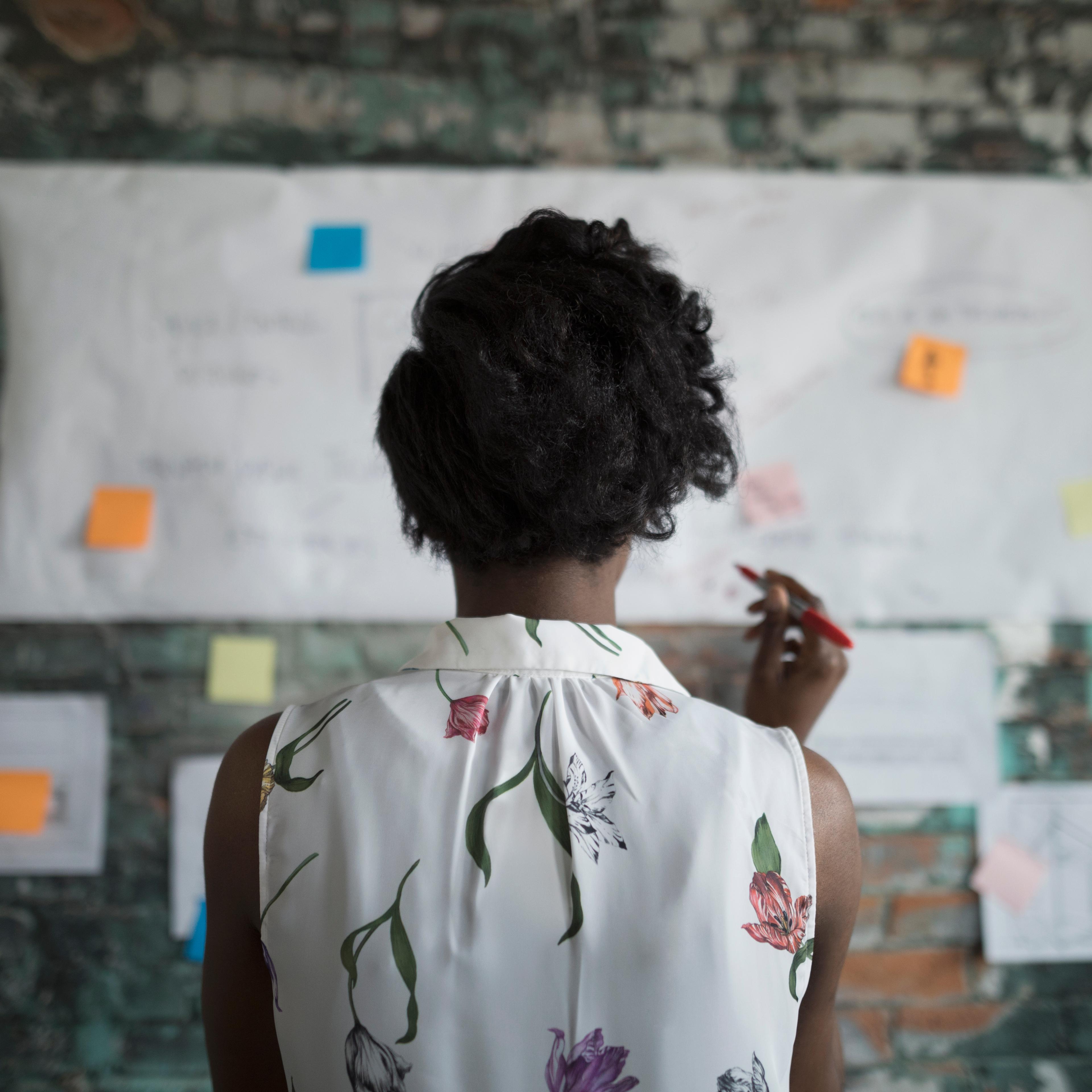 Creative businesswoman brainstorming, reviewing flow chart hanging on brick wall in office