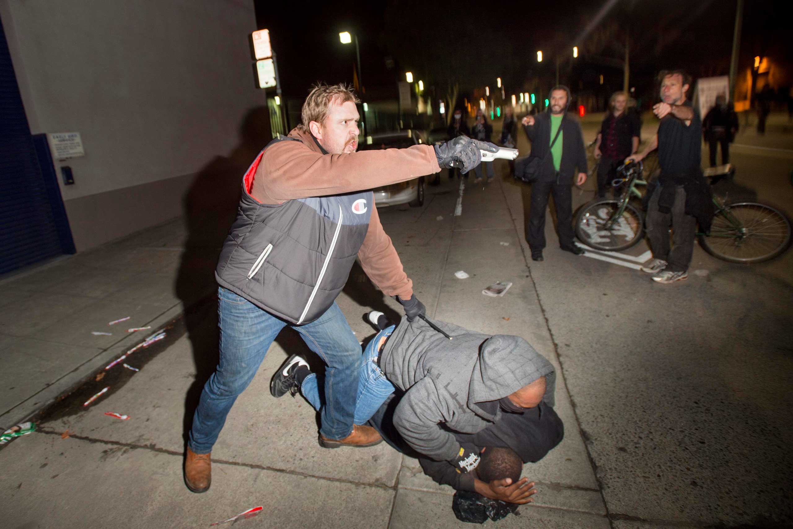 An undercover police officer, who had been marching with anti-police demonstrators, aims his gun at protesters after some in the crowd attacked him and his partner in Oakland