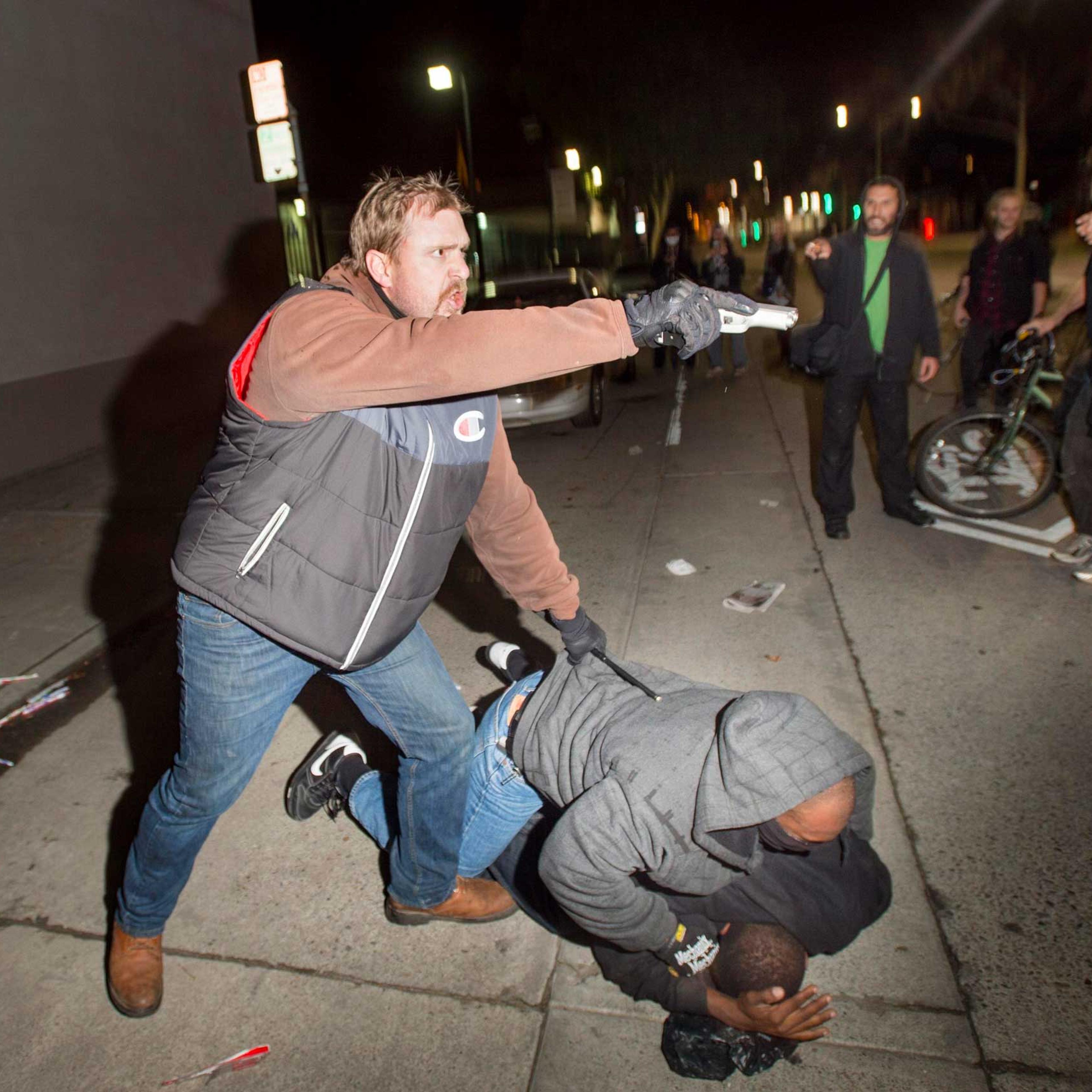 An undercover police officer, who had been marching with anti-police demonstrators, aims his gun at protesters after some in the crowd attacked him and his partner in Oakland