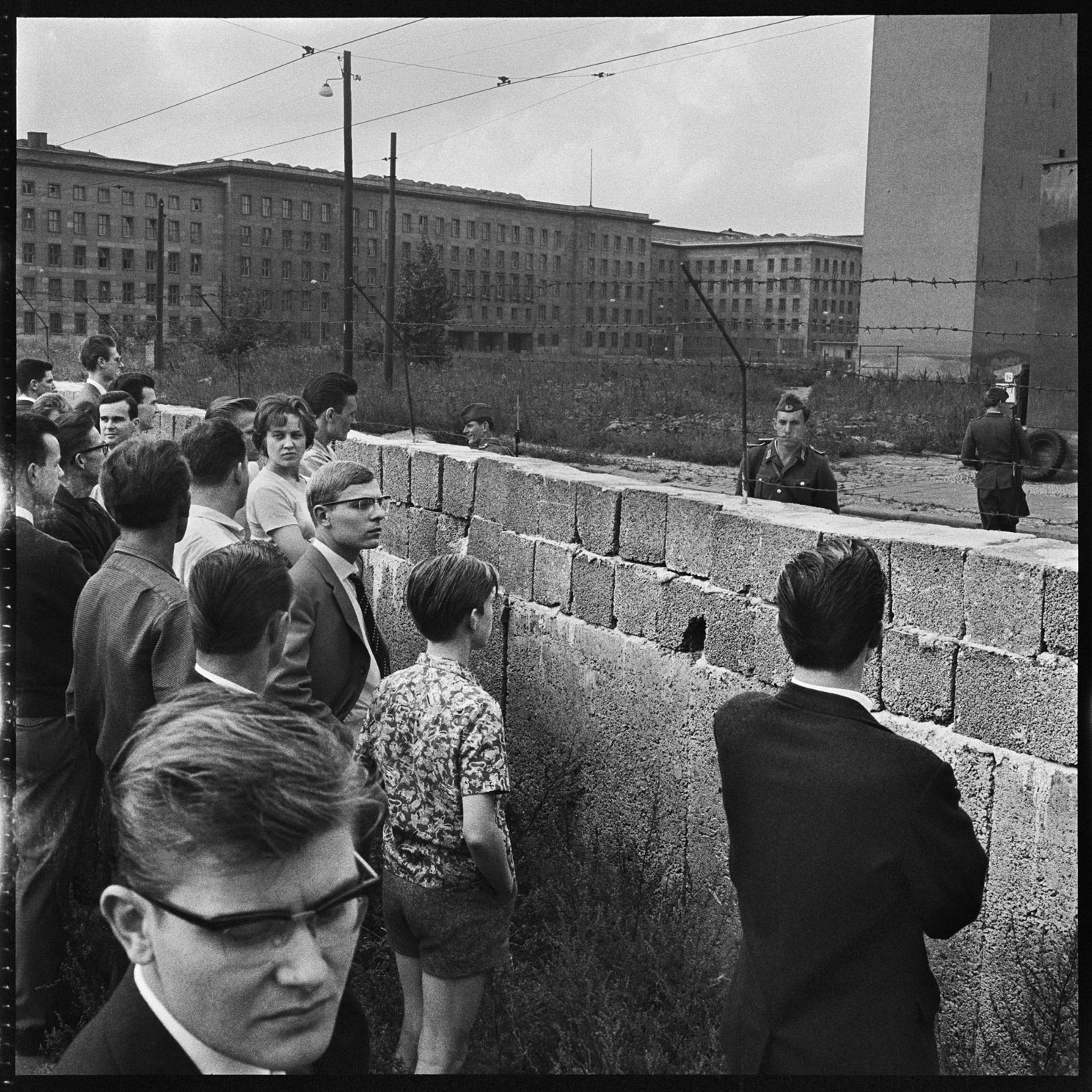 West Berliners looking over a portion of the Berlin Wall at the time of its construction. East German soldiers looking back, West Berlin, Germany, August 1961.