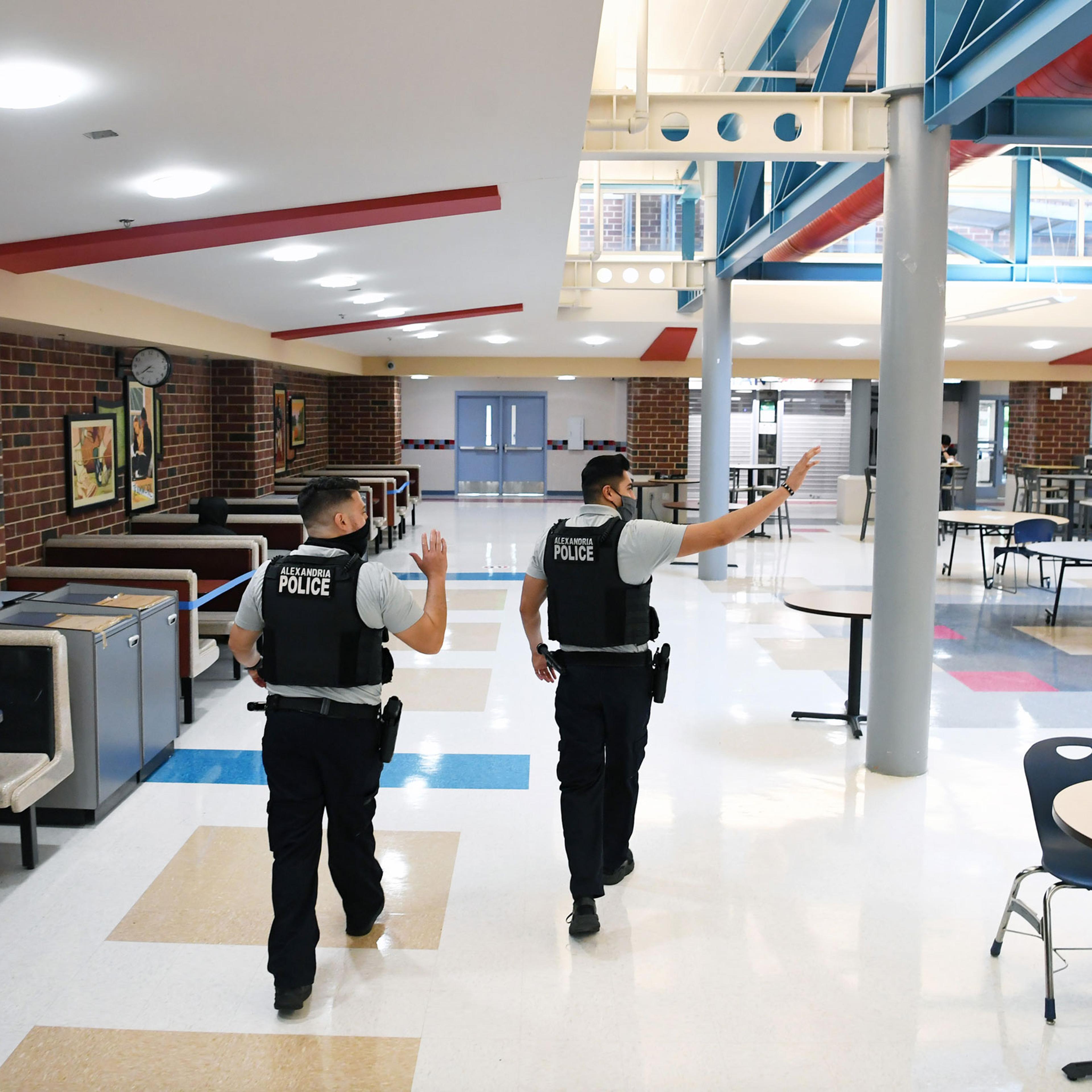Alexandria Police Department school resource officers wave to students as they walk through the cafeteria