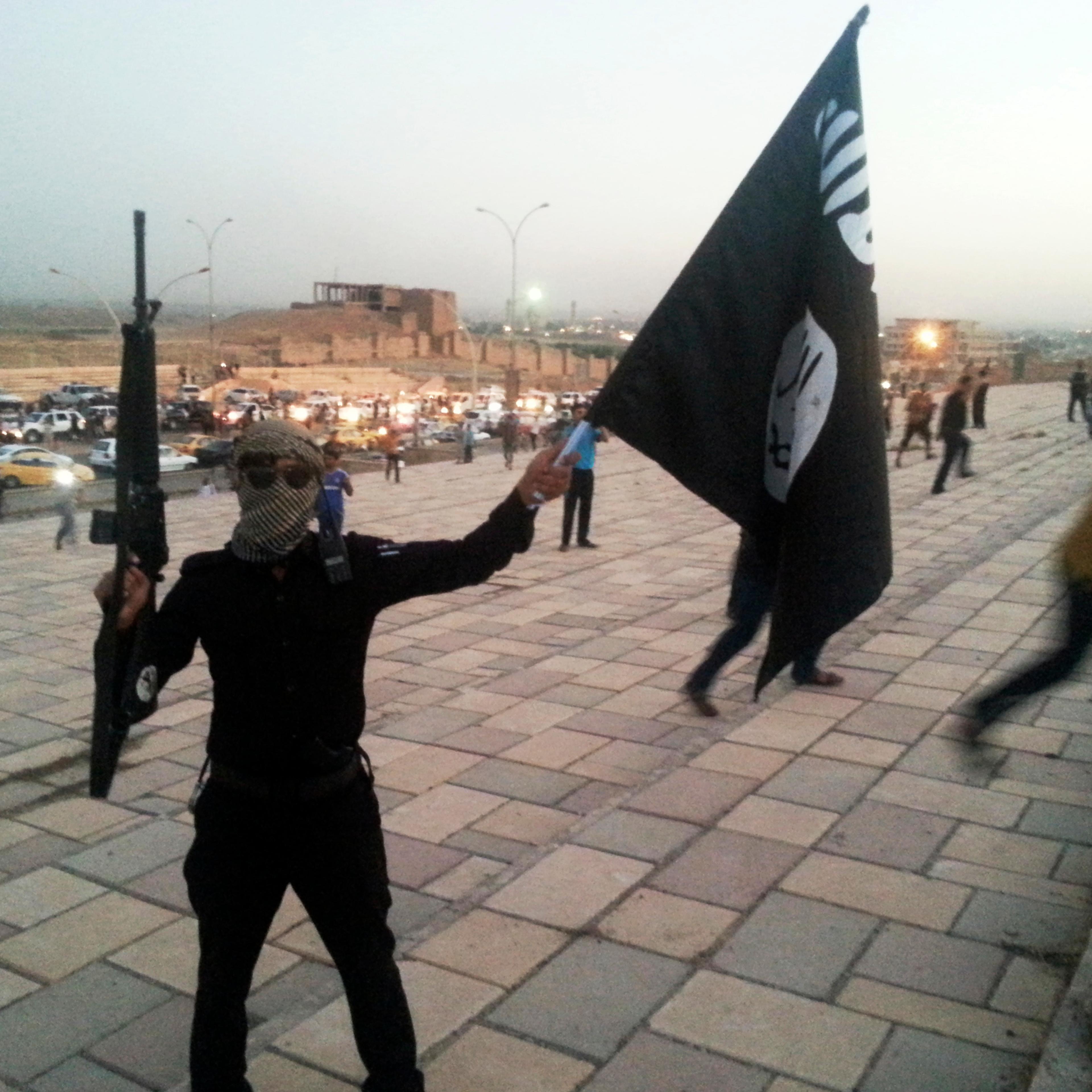 A fighter of the ISIL holds a flag and a weapon on a street in Mosul