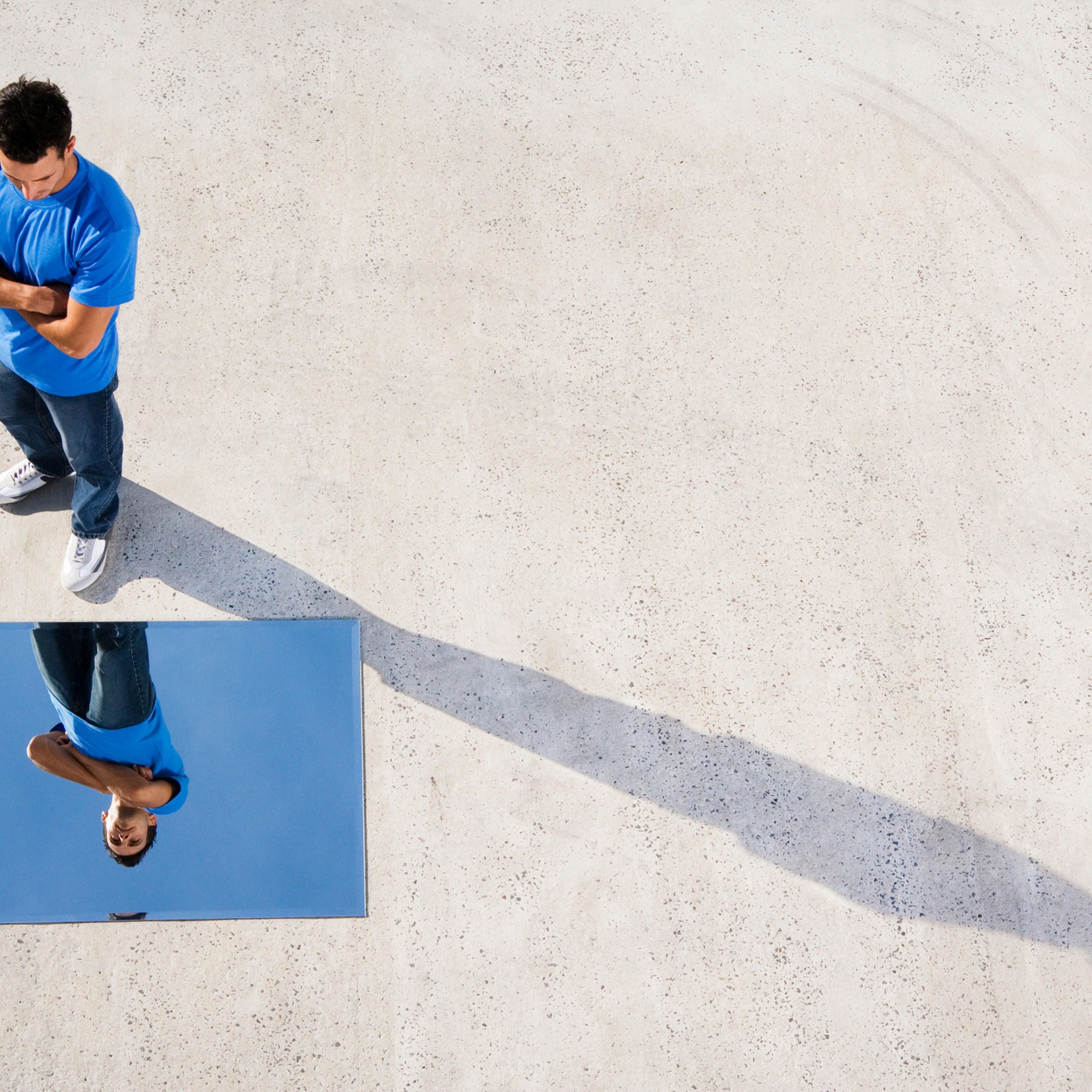 Man standing with mirror on ground and reflection