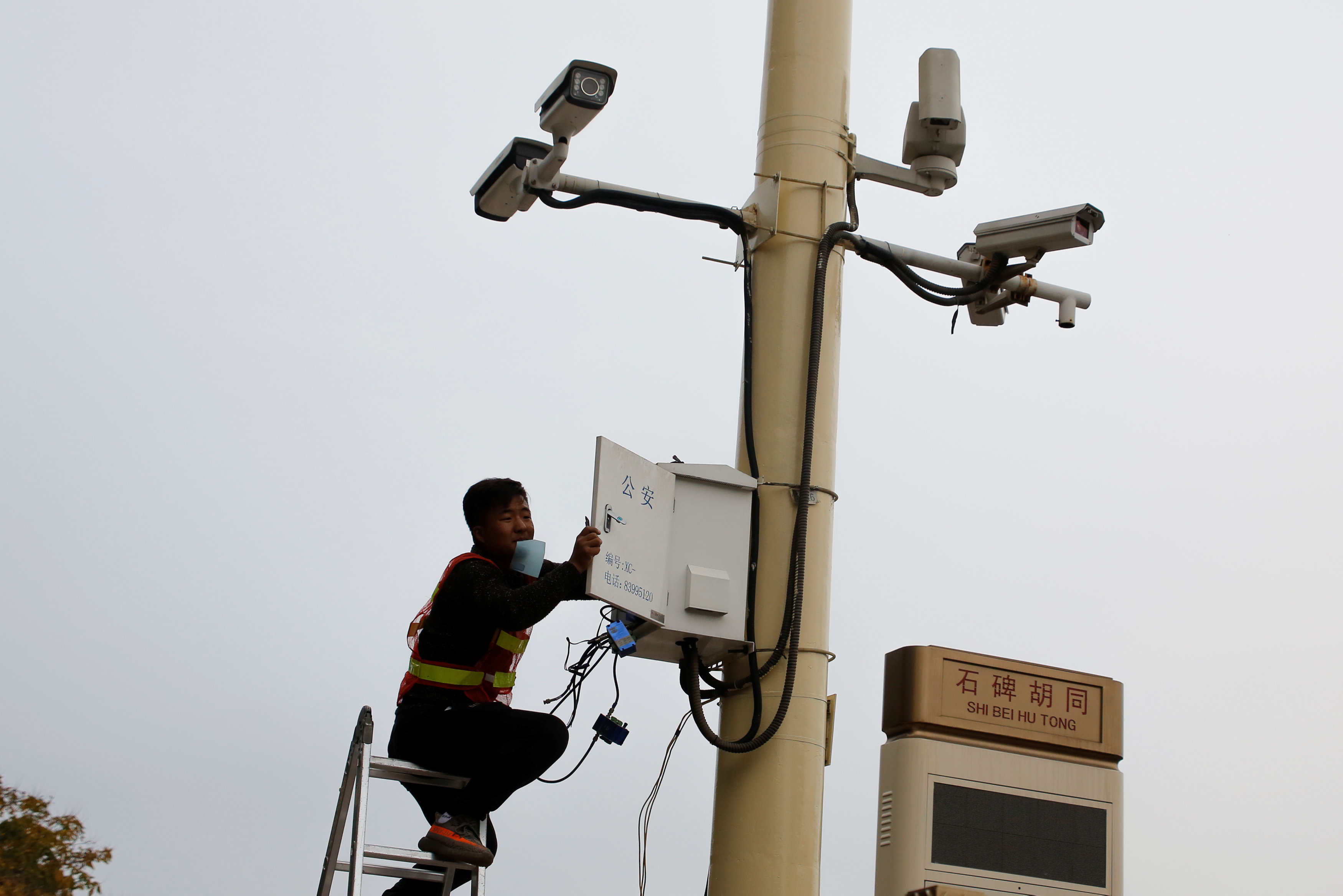 A man works on electrical wires in a box underneath surveillance cameras at Tiananmen Square in Beijing