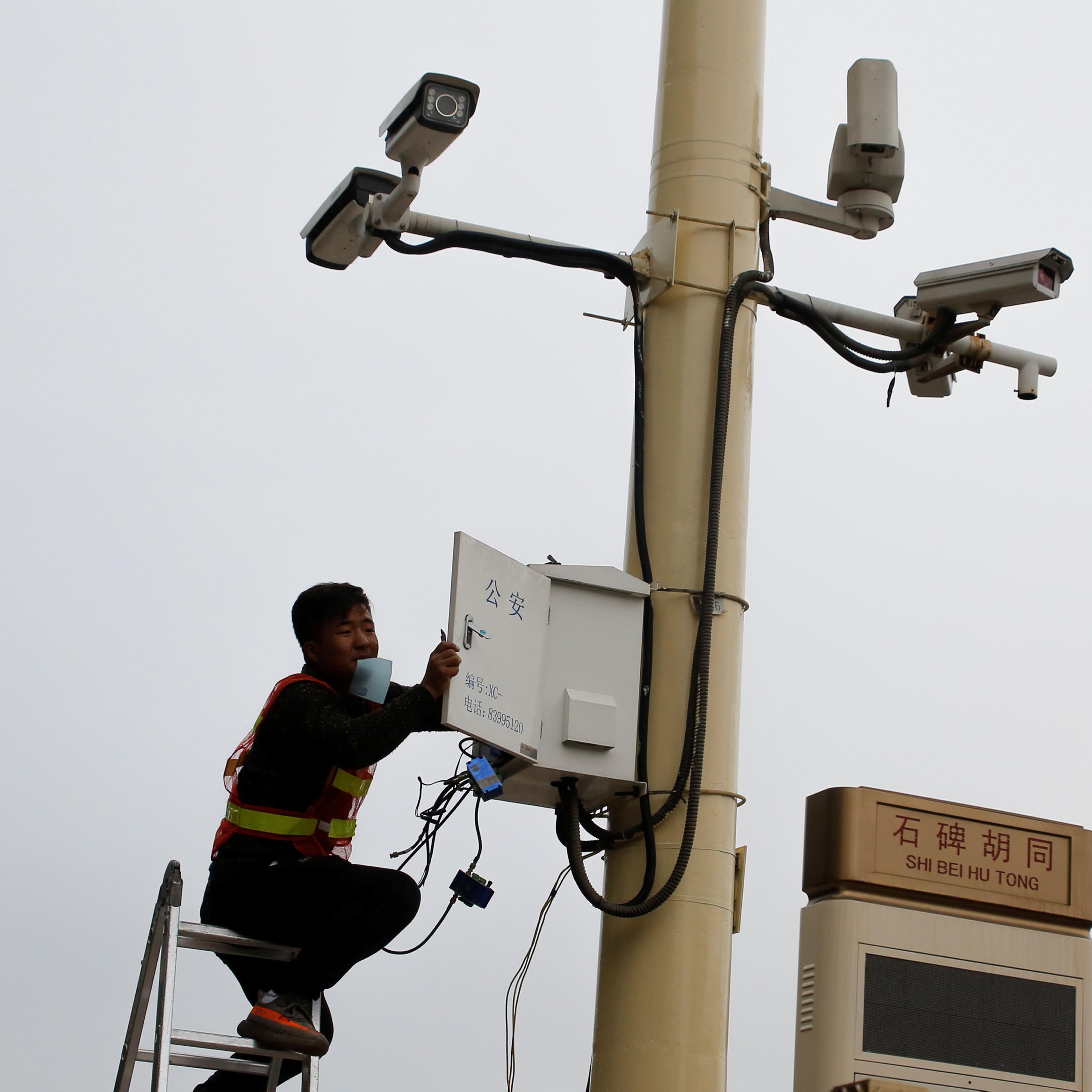 A man works on electrical wires in a box underneath surveillance cameras at Tiananmen Square in Beijing