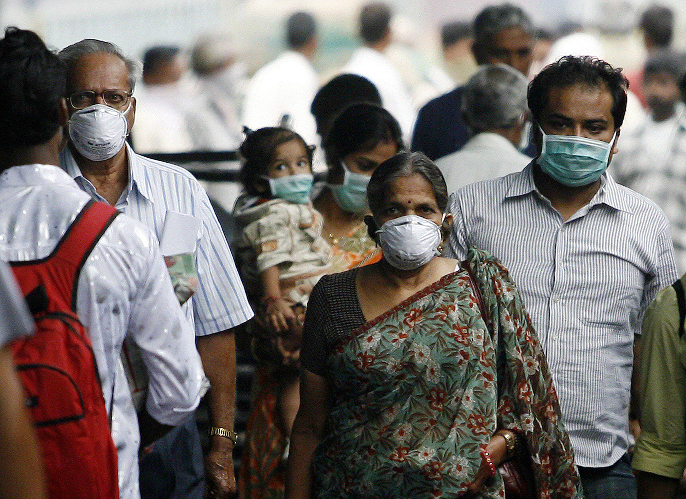 Travellers with masks walk on a railway platform in Pune