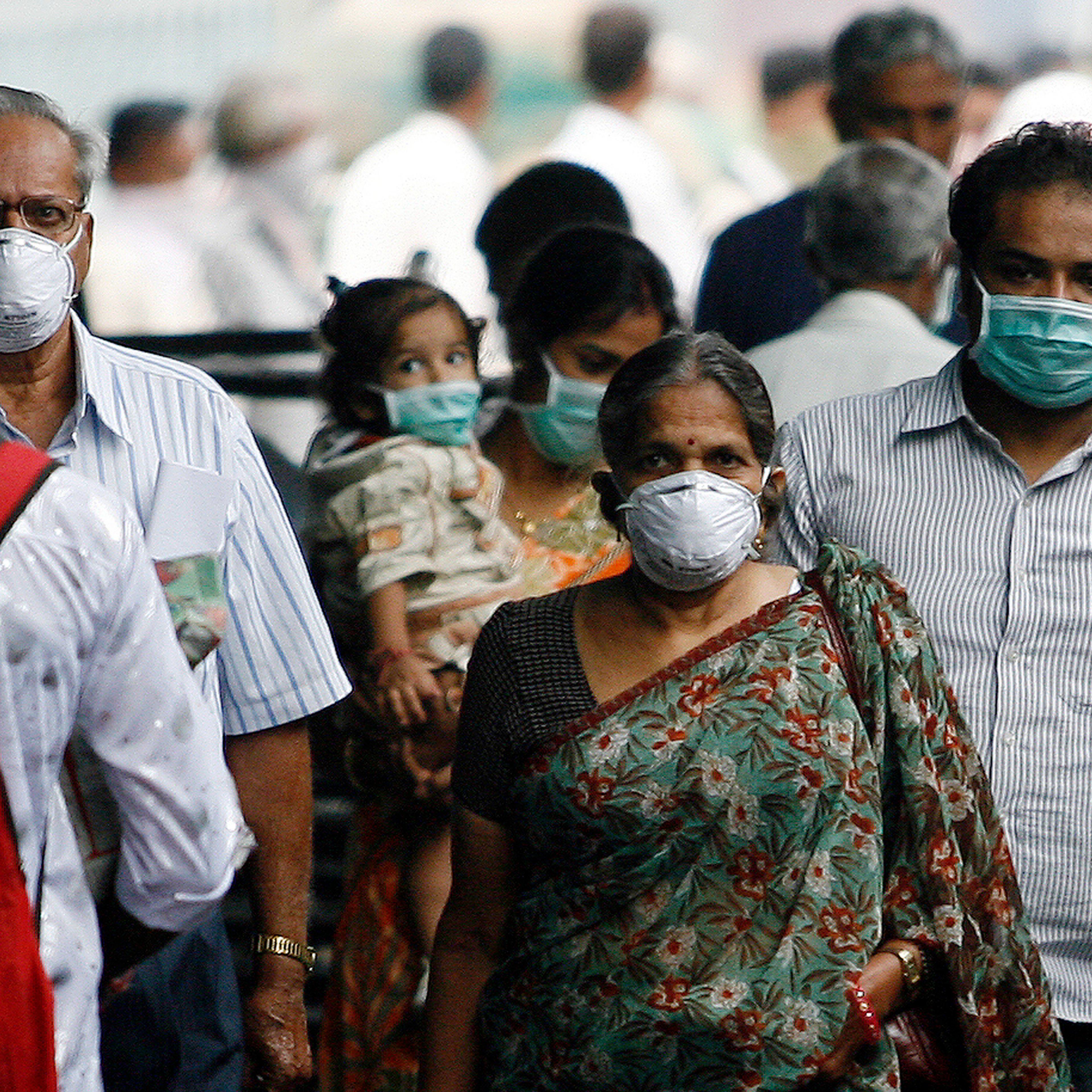 Travellers with masks walk on a railway platform in Pune