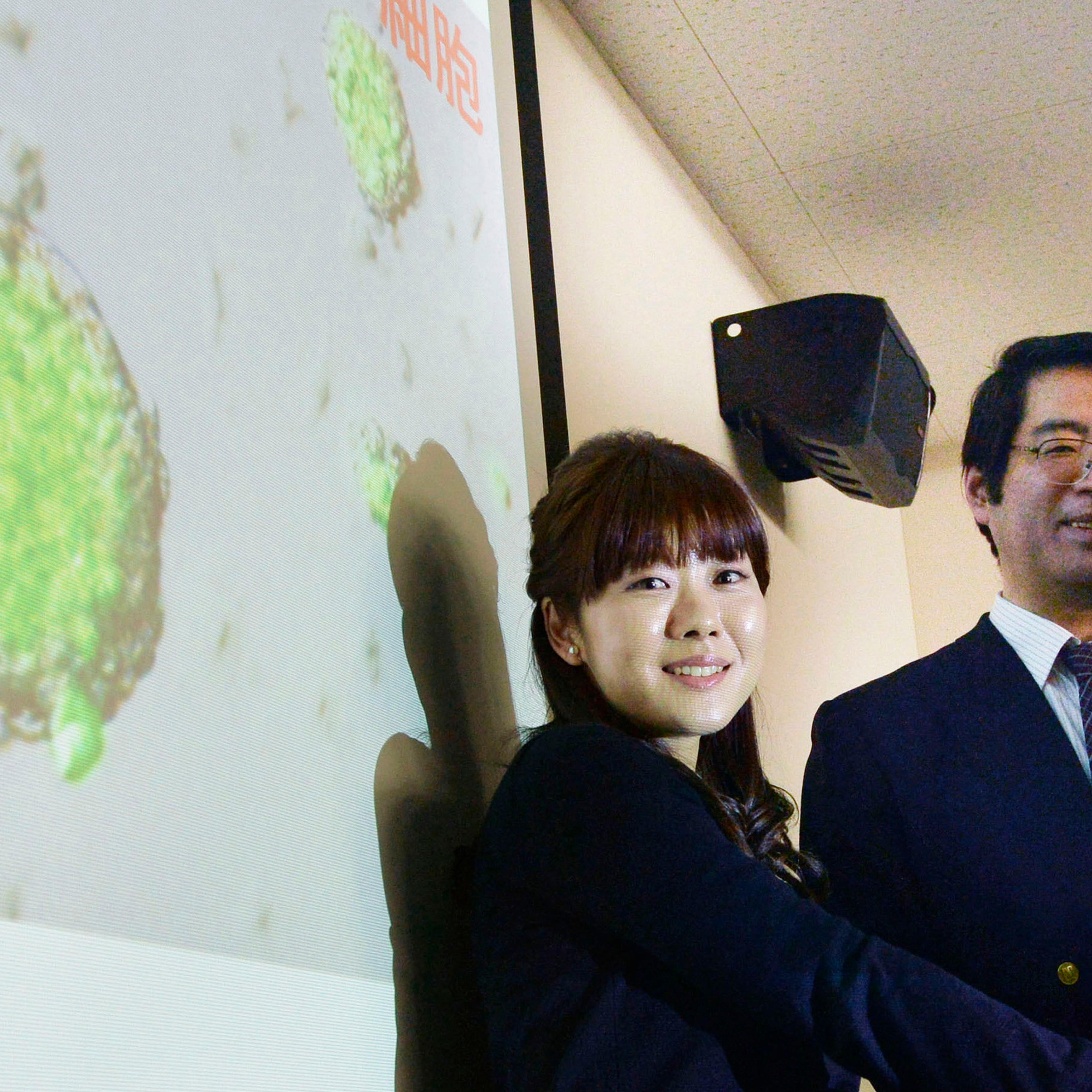 Sasai, deputy director of the Riken's Center for Developmental Biology, poses for a photo with Haruko Obokata in front of a screen showing STAP cells, in Kobe