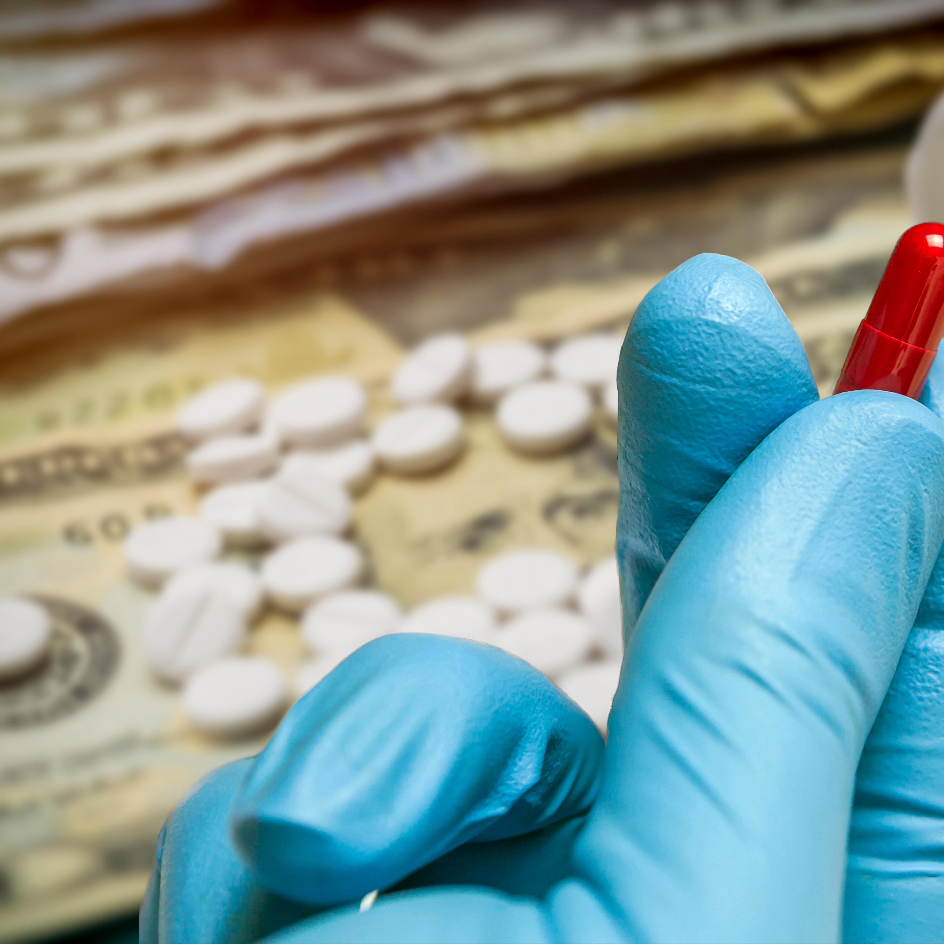 Hand holding up a red capsule with dollar bills in the background.