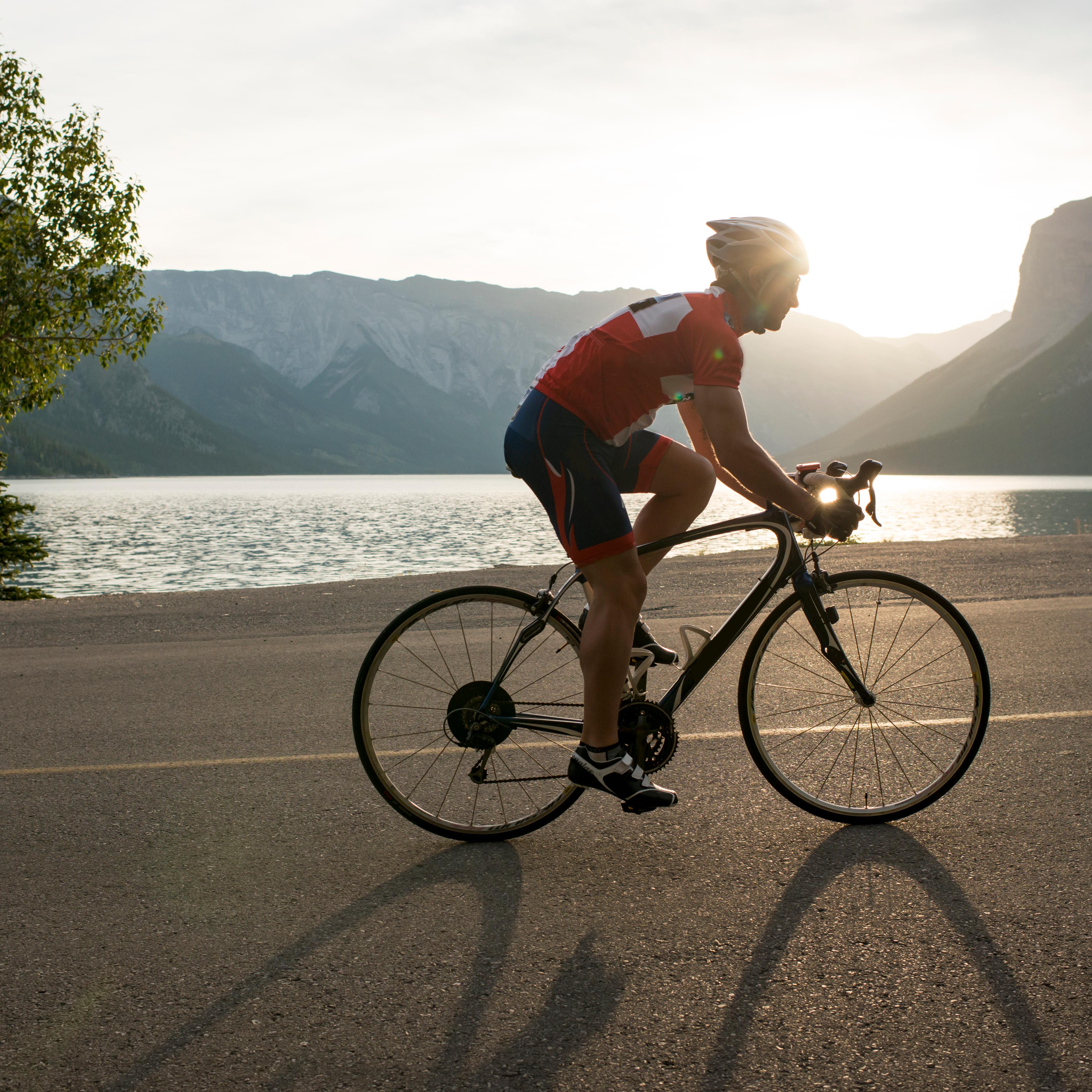 Road biker follows mountain road, sunrise