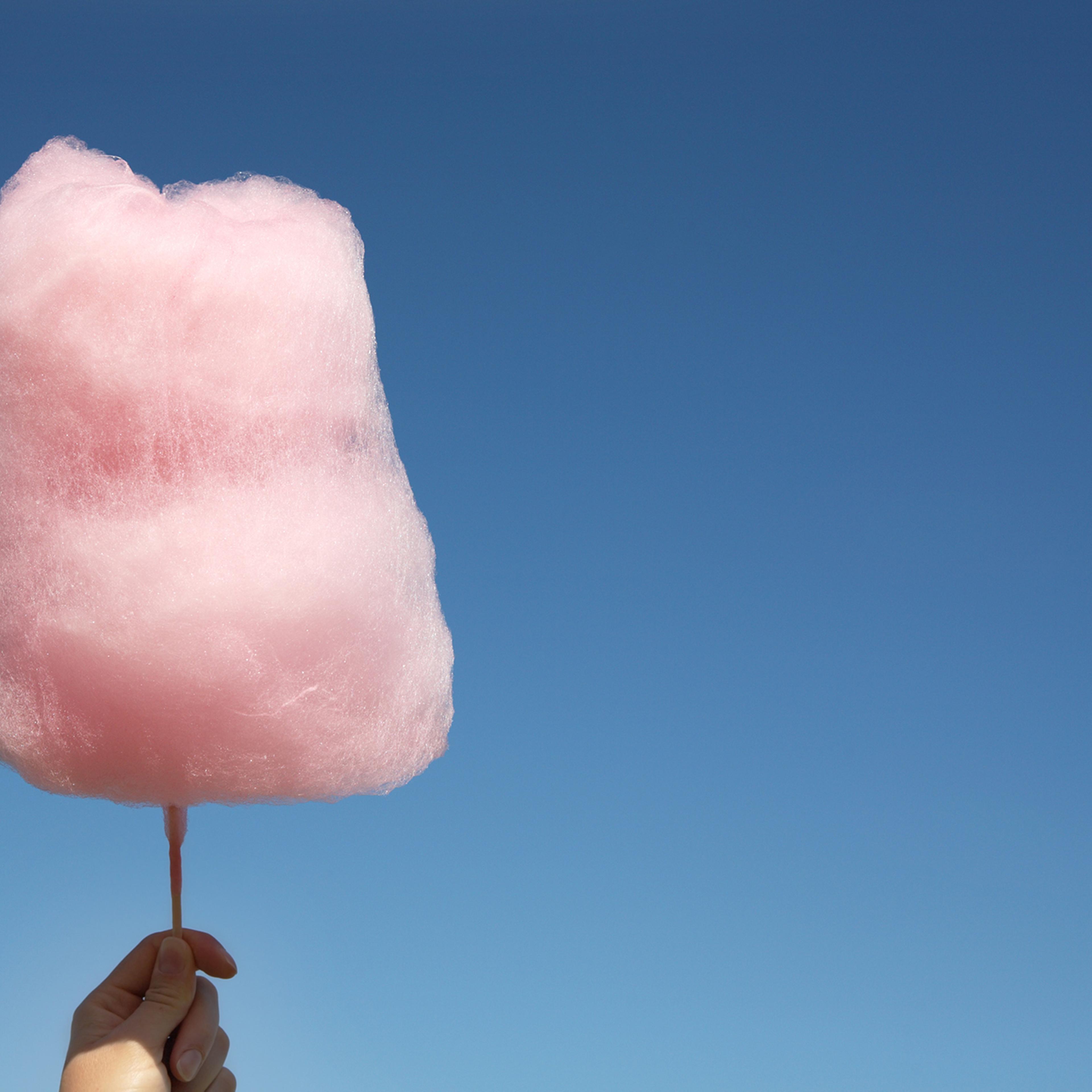 Pink cotton candy being held up against a clear blue sky
