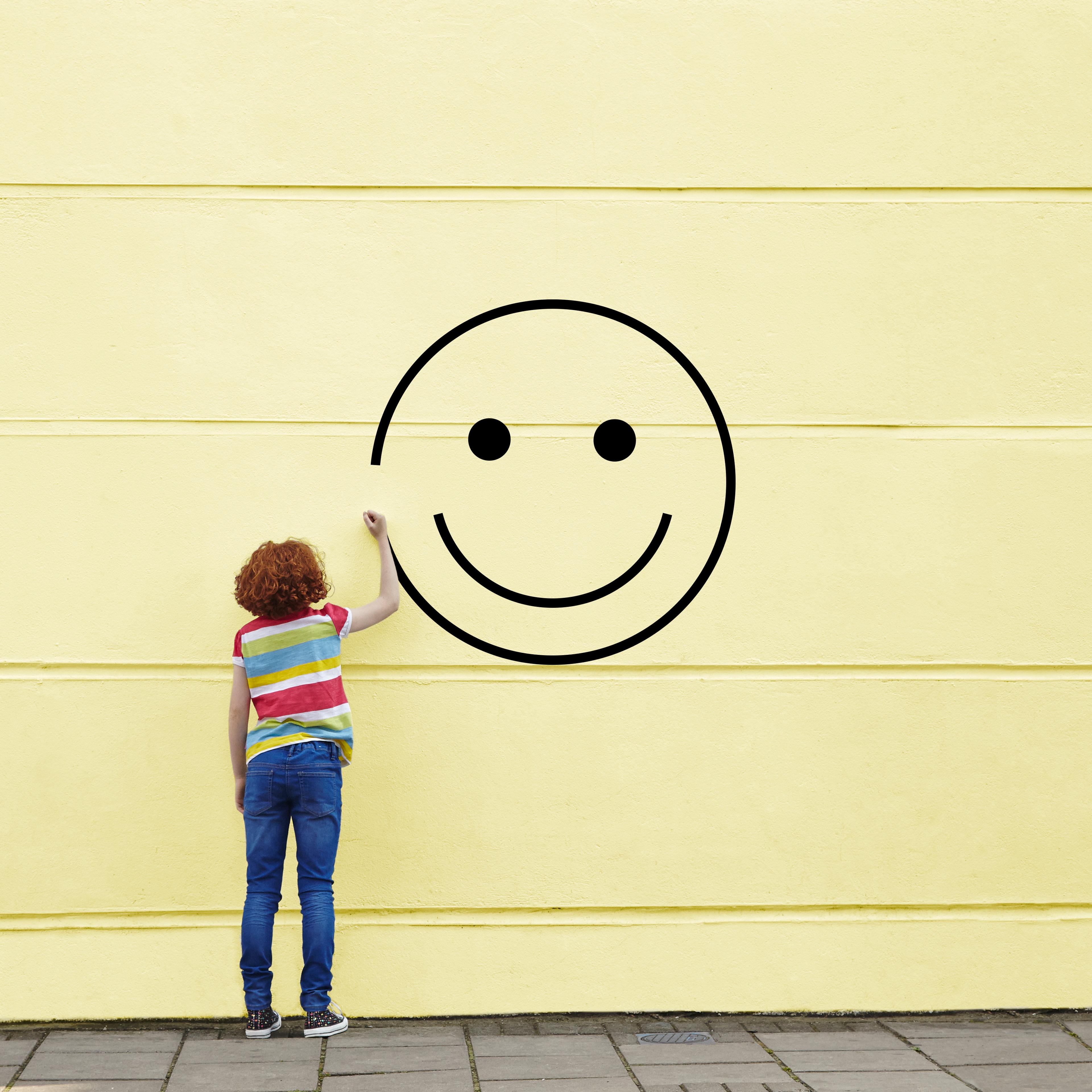 Girl drawing smiley face on to a wall