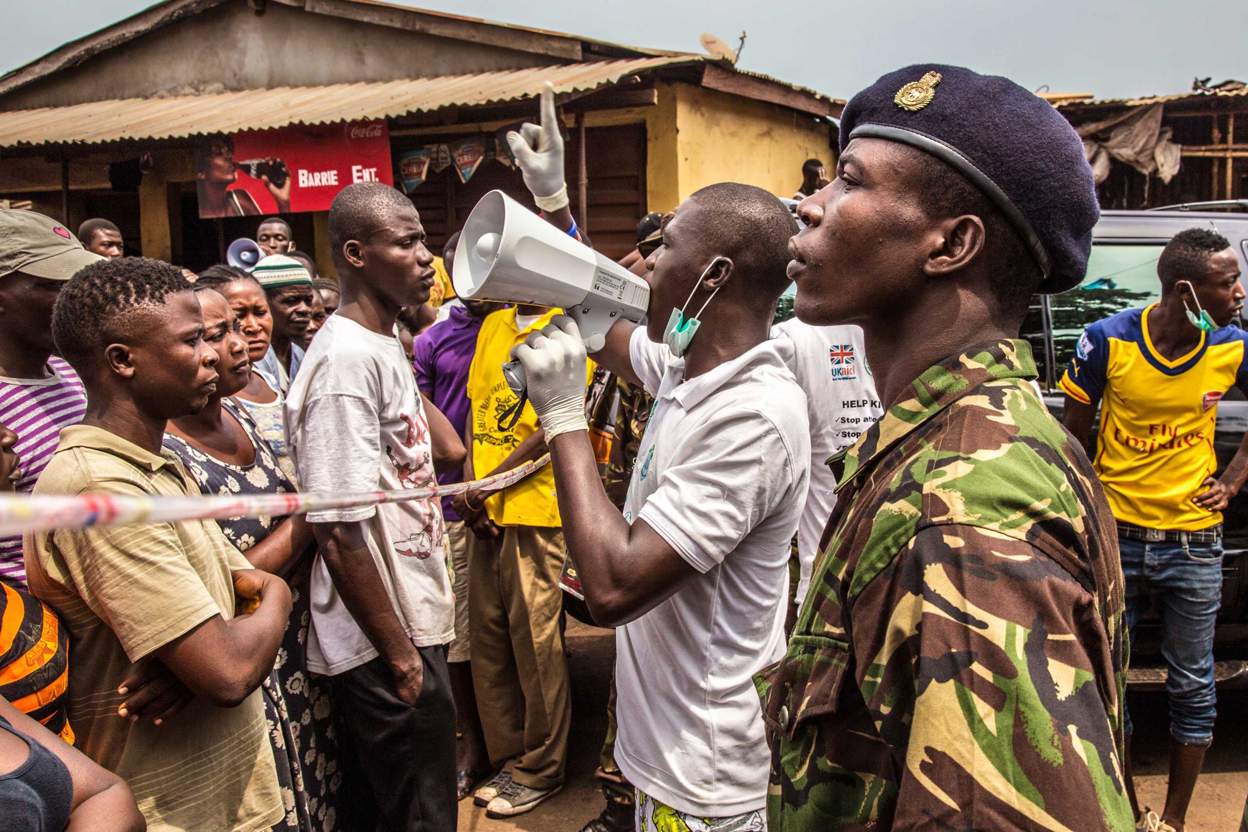 People stand in line for food to be distributed to them as a health worker makes an announcement in Freetown, Sierra Leone on March 27, 2015.