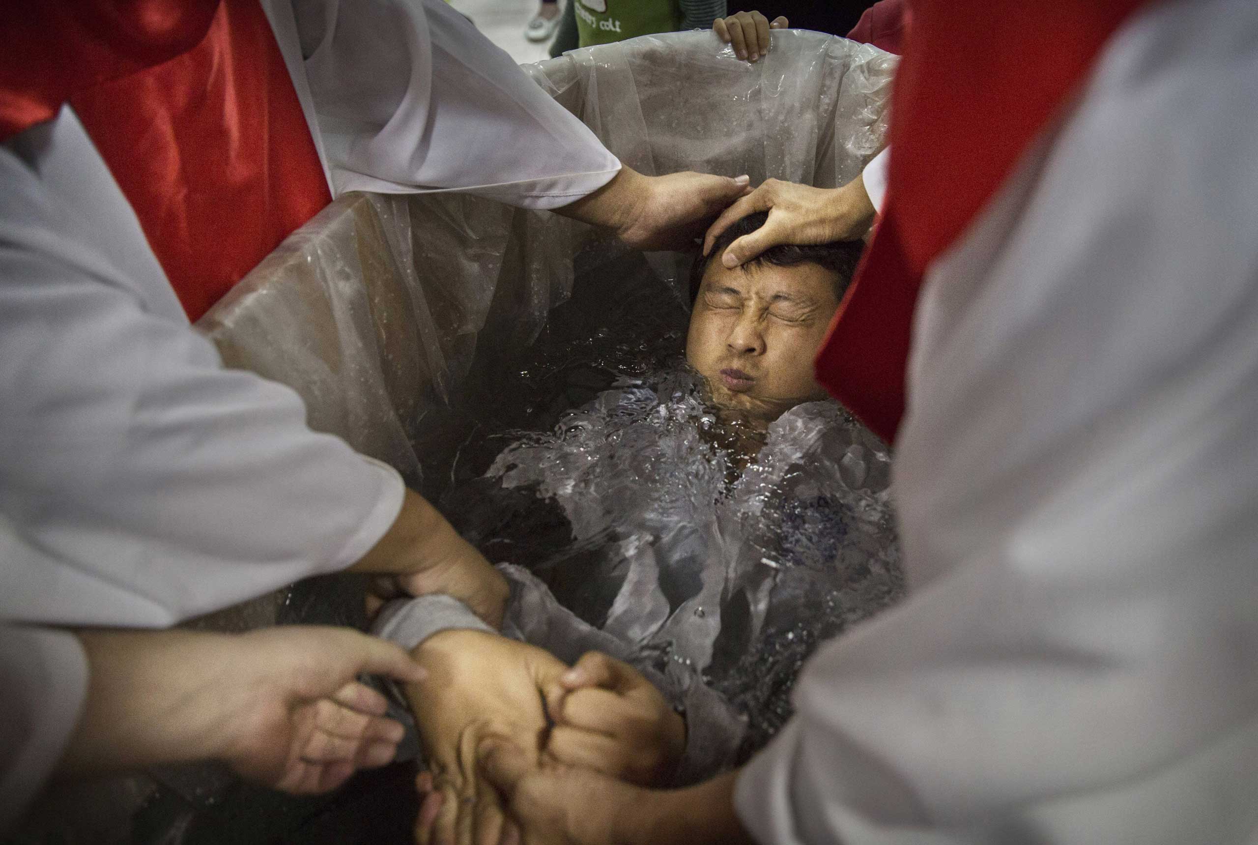 A new Christian man is dunked in the water in a small tub as he is baptized.