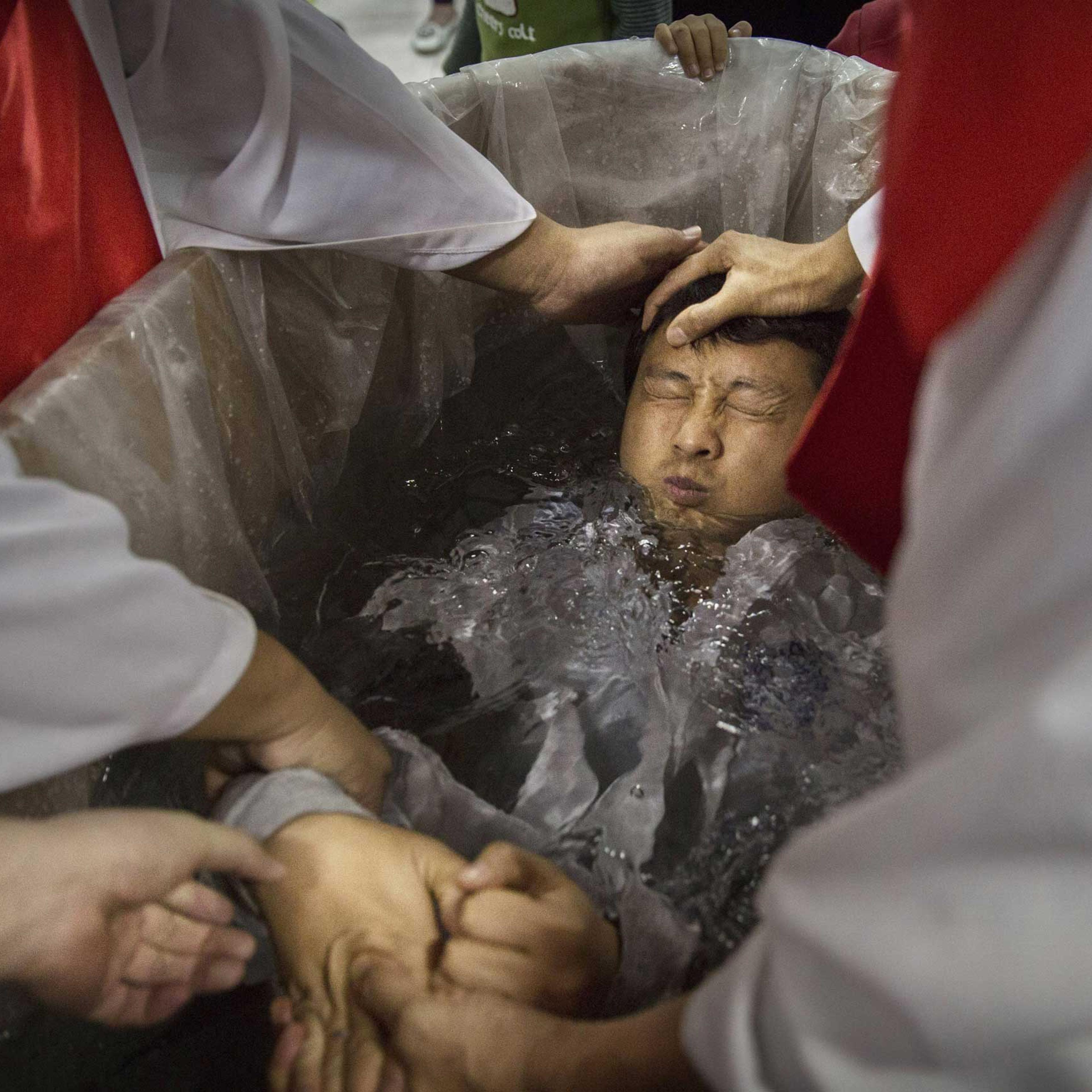 A new Christian man is dunked in the water in a small tub as he is baptized.