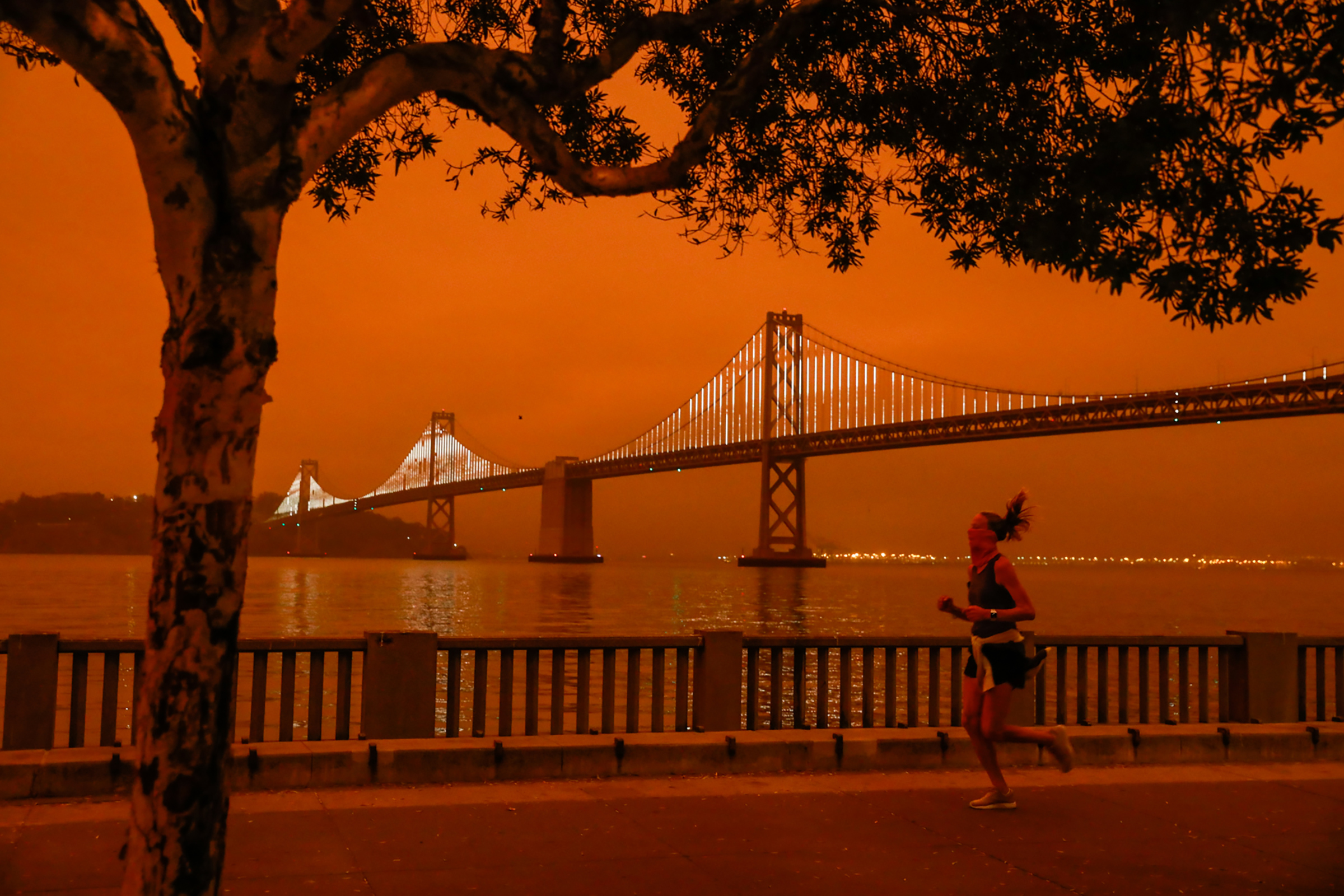 A woman jogs by the Bay Bridge as dark orange skies hang over downtown San Francisco on Sept. 9, 2020 due to multiple wildfires burning across California and Oregon.