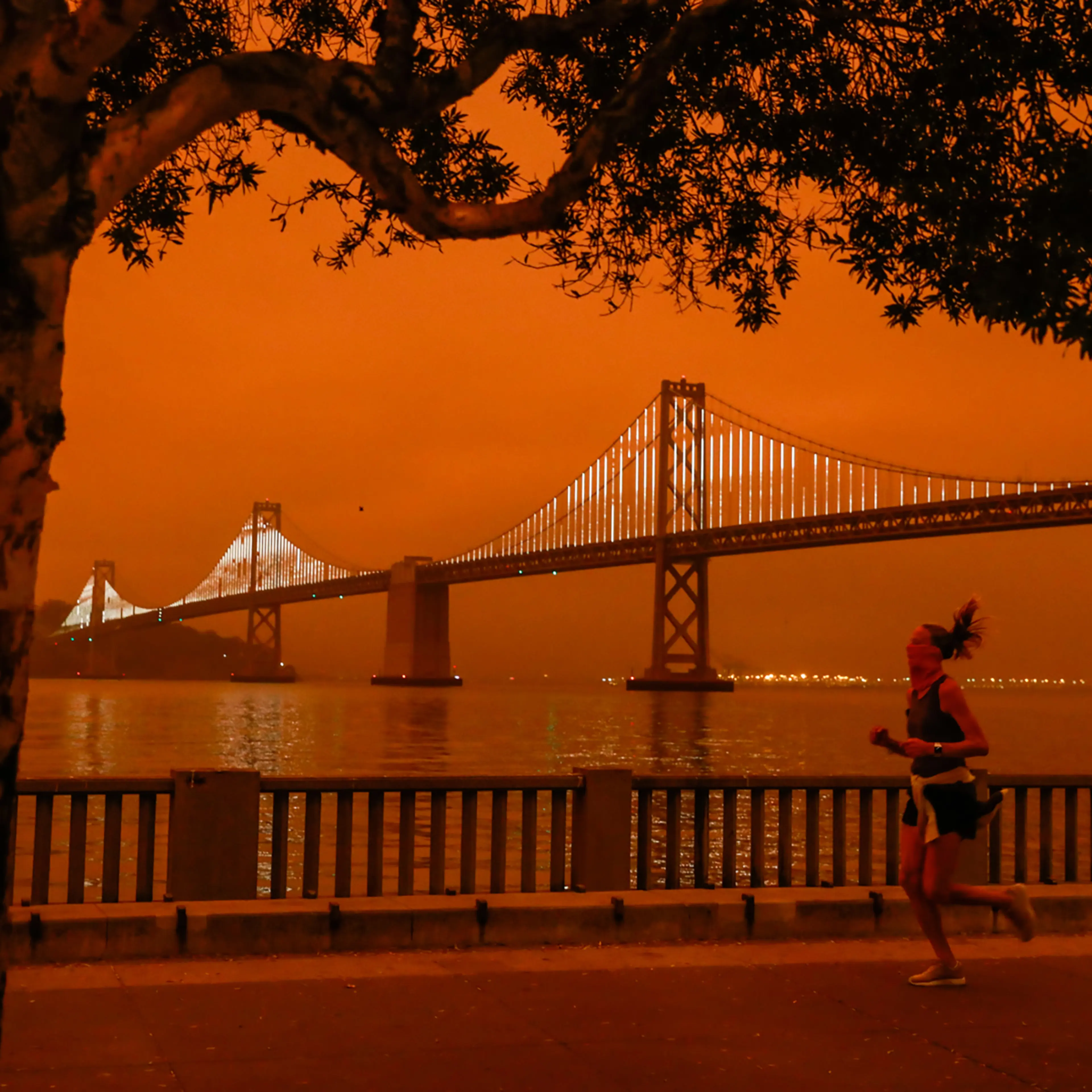 A woman jogs by the Bay Bridge as dark orange skies hang over downtown San Francisco on Sept. 9, 2020 due to multiple wildfires burning across California and Oregon.