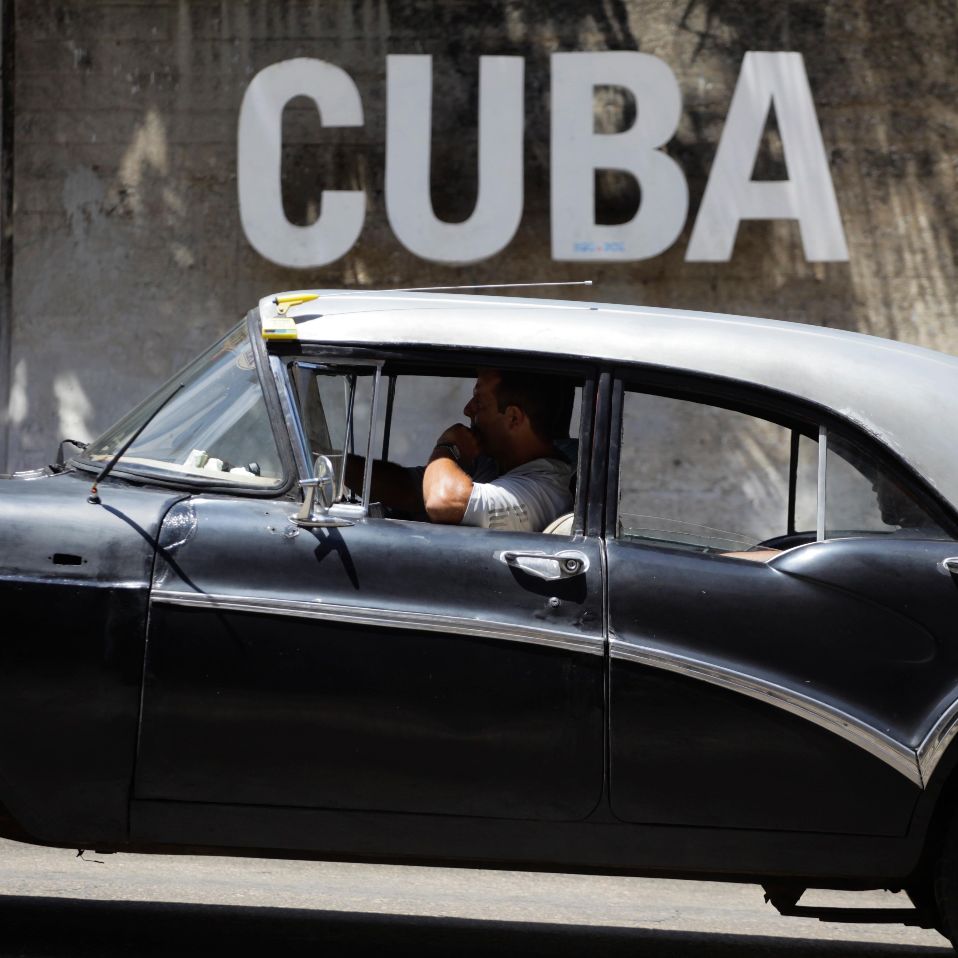 A man drives his taxi past a Cultural Center with the word "Cuba" on it, in Havana, Cuba,, April 14, 2015