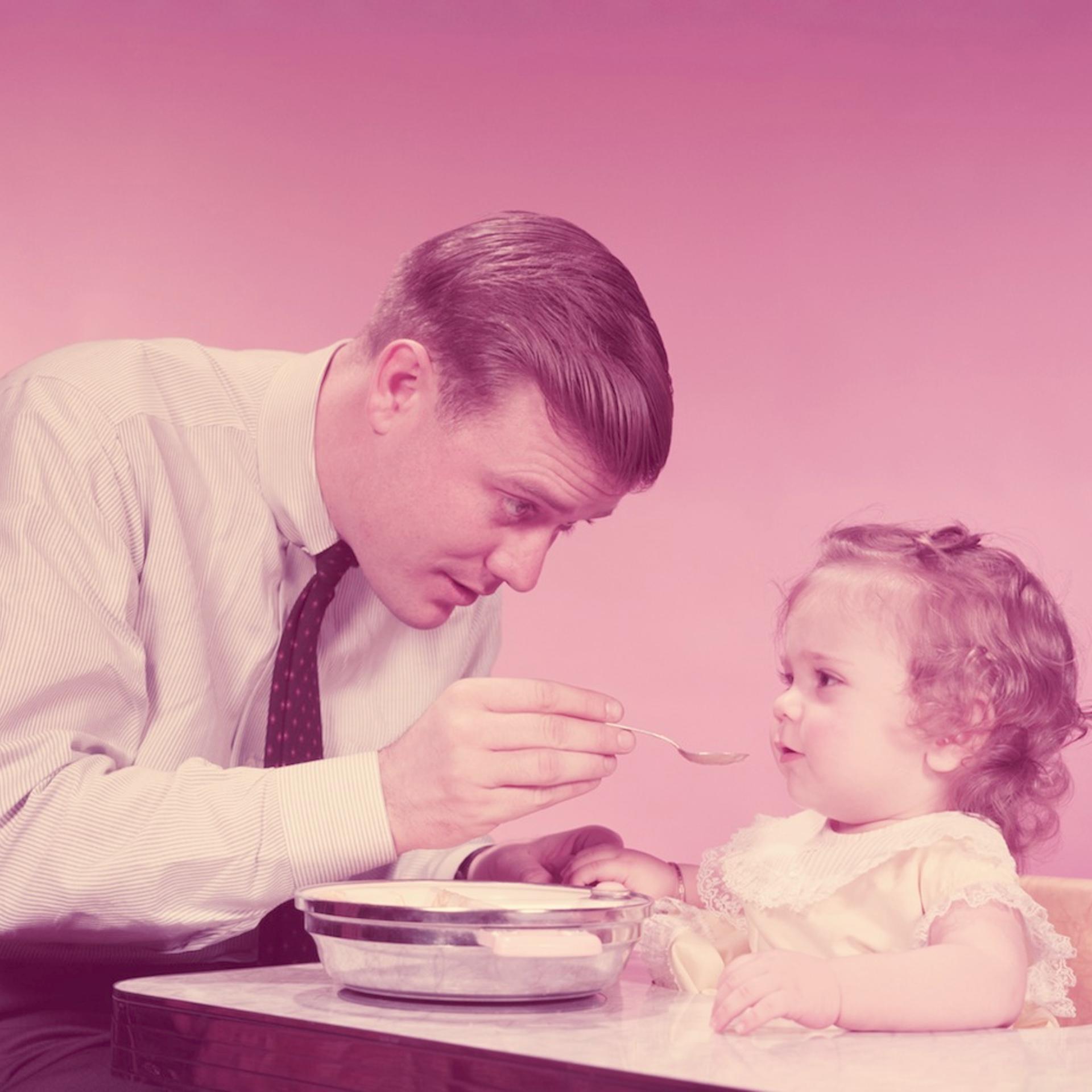 Father feeding daughter sitting in high chair