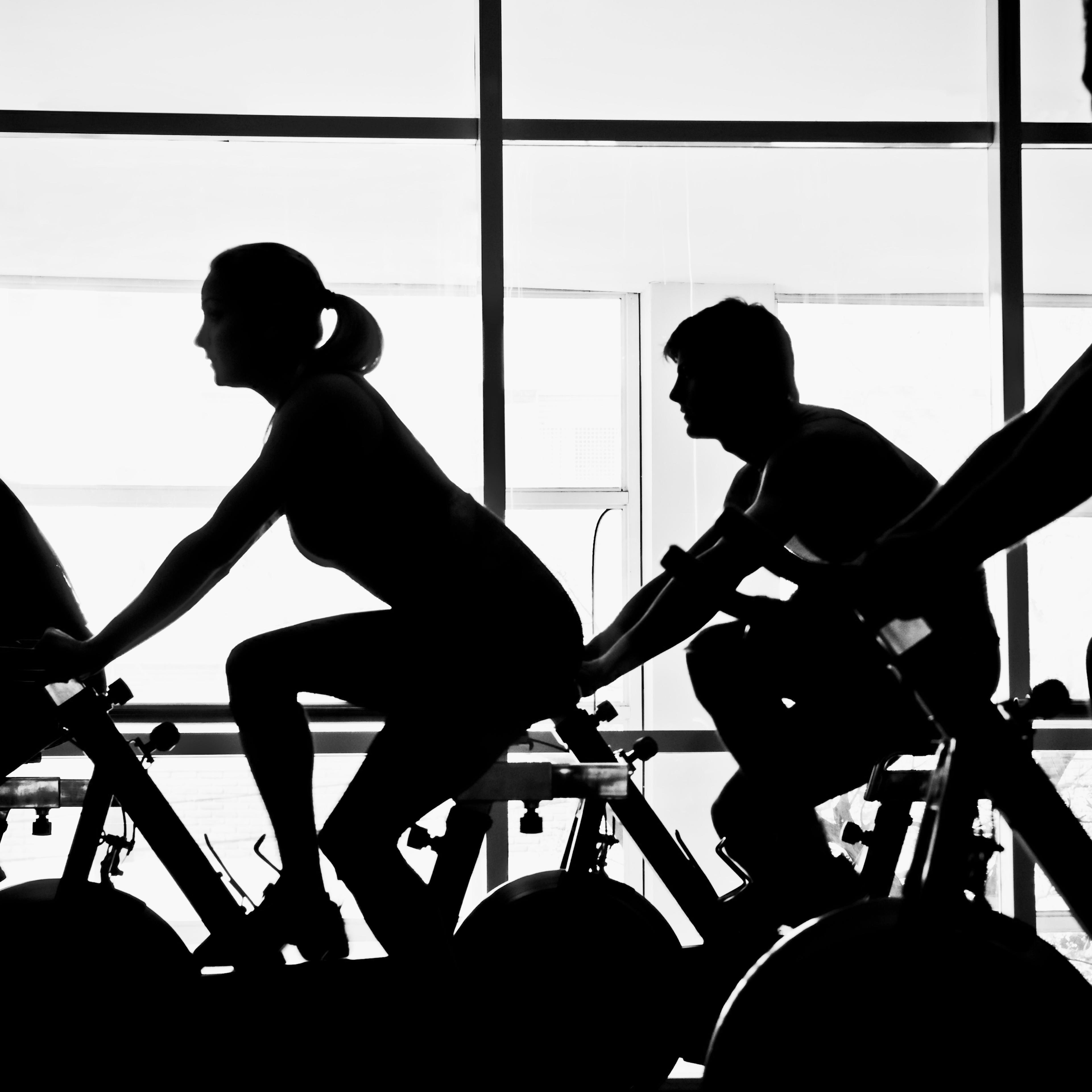 Silhouette of four people working out on exercise bikes in a gym