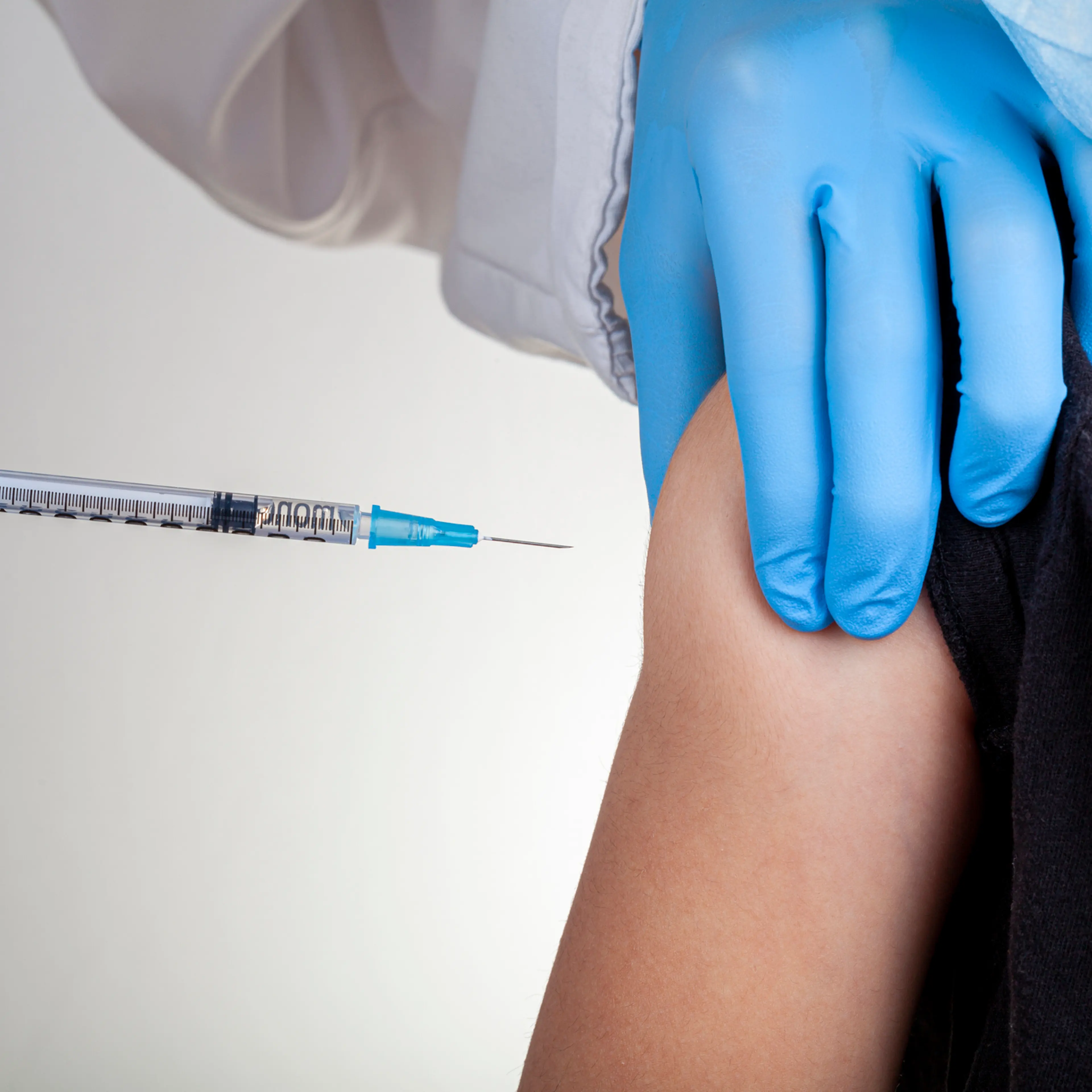 A health care professional wearing gloves and white coat is administering a childhood vaccine.
