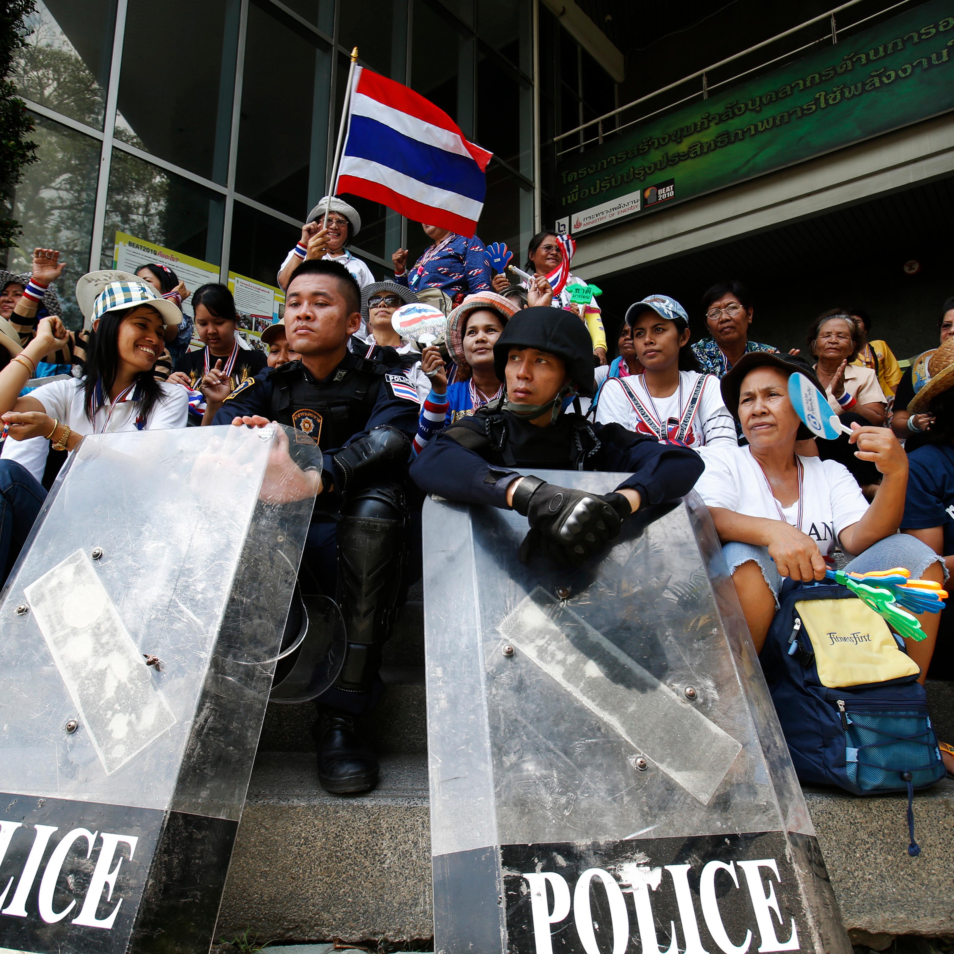 Anti-government protesters sit with riot policemen outside the NBT TV station in Bangkok