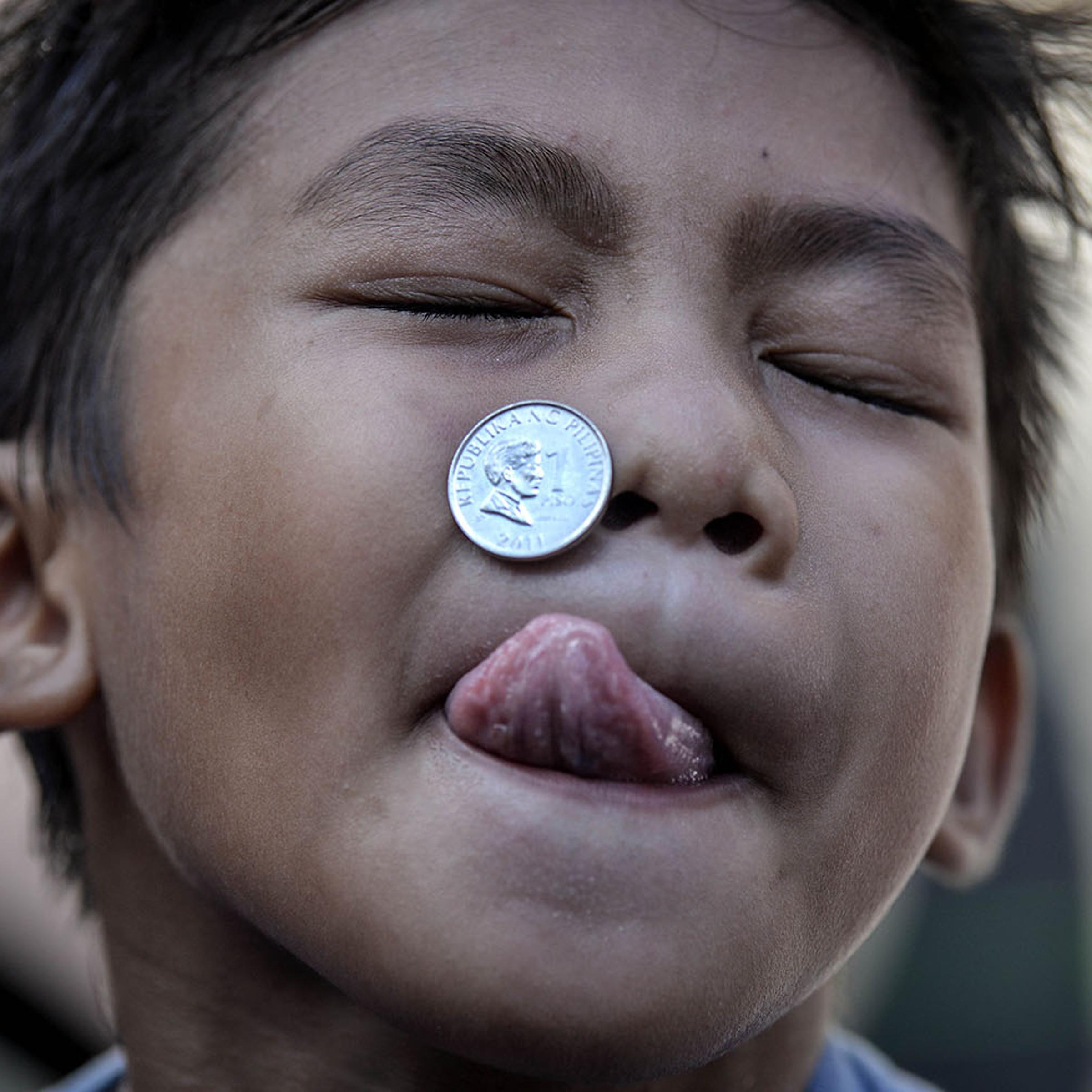 A boy contorts his face as he competes in a parlor game trying to move a coin from his forehead to his mouth as part of the feast day of Saint Rita of Cascia in Paranaque, Philippines, on May 18, 2014.