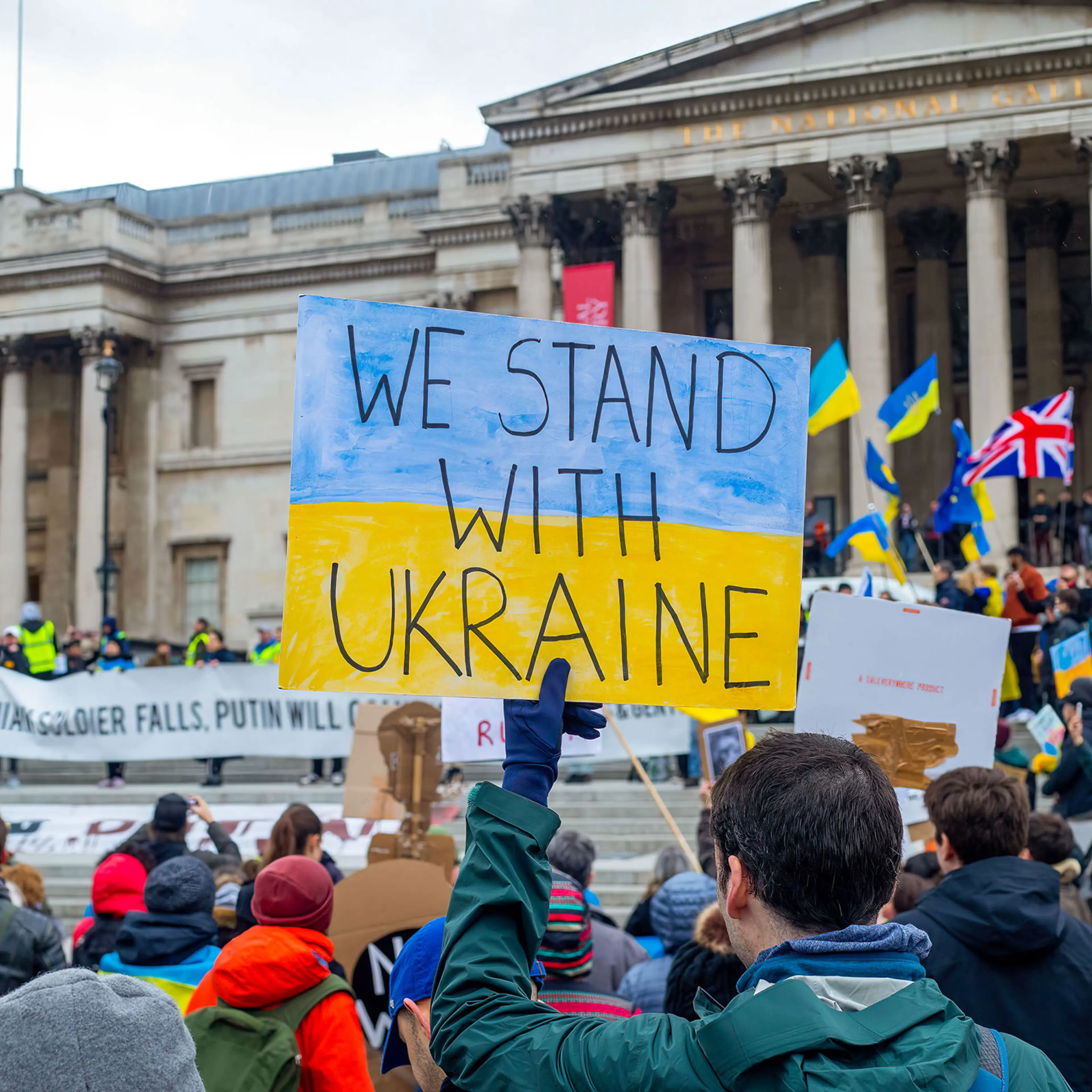 A protester holds a sign saying "We Stand With Ukraine"