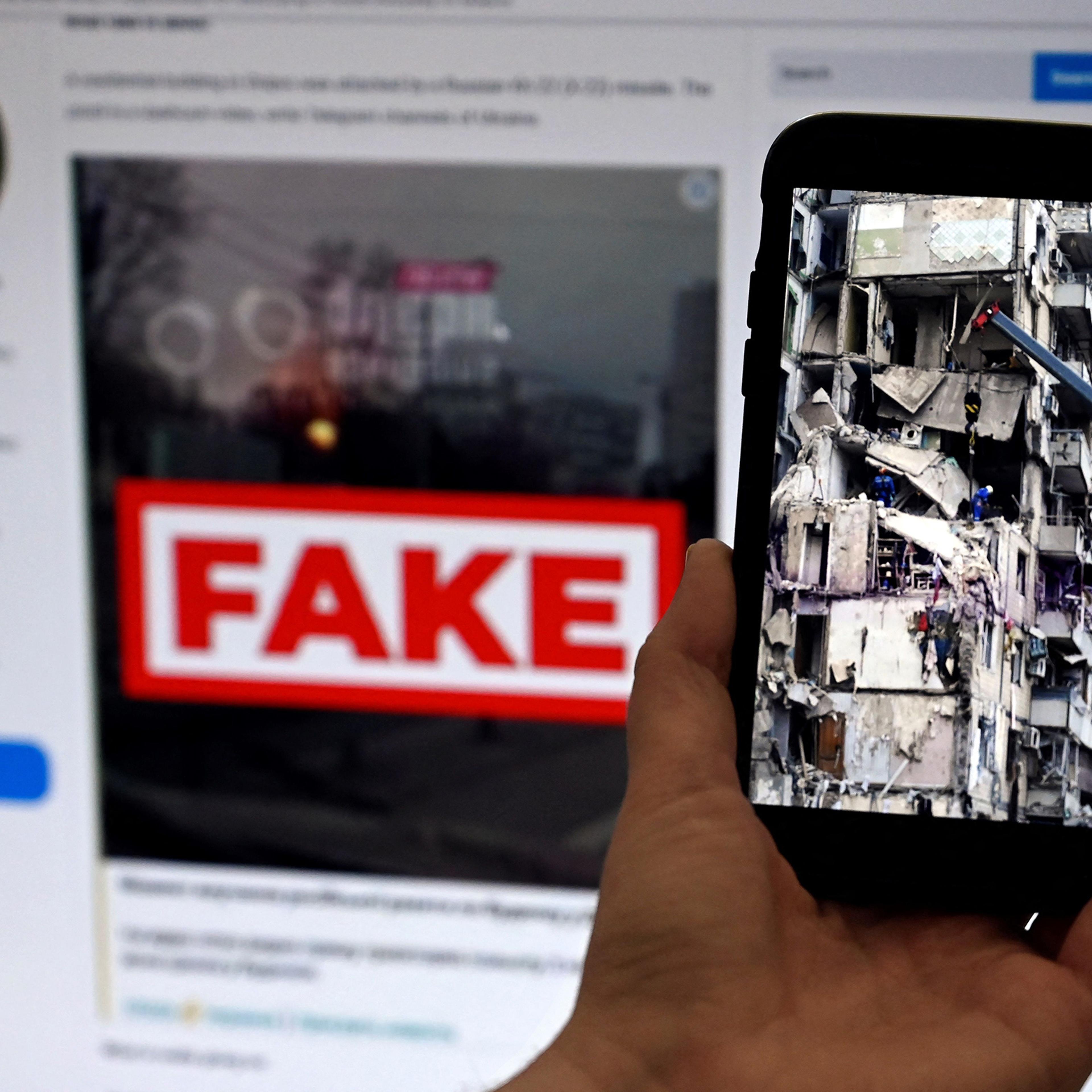 This photo-illustration taken on Feb. 14 shows a phone screen displaying a picture of rescuers working on a residential building destroyed after a missile strike, in Dnipro on Jan. 16, with the WarOnFakes.com website displaying a fake video of the same residential building shown in the background.