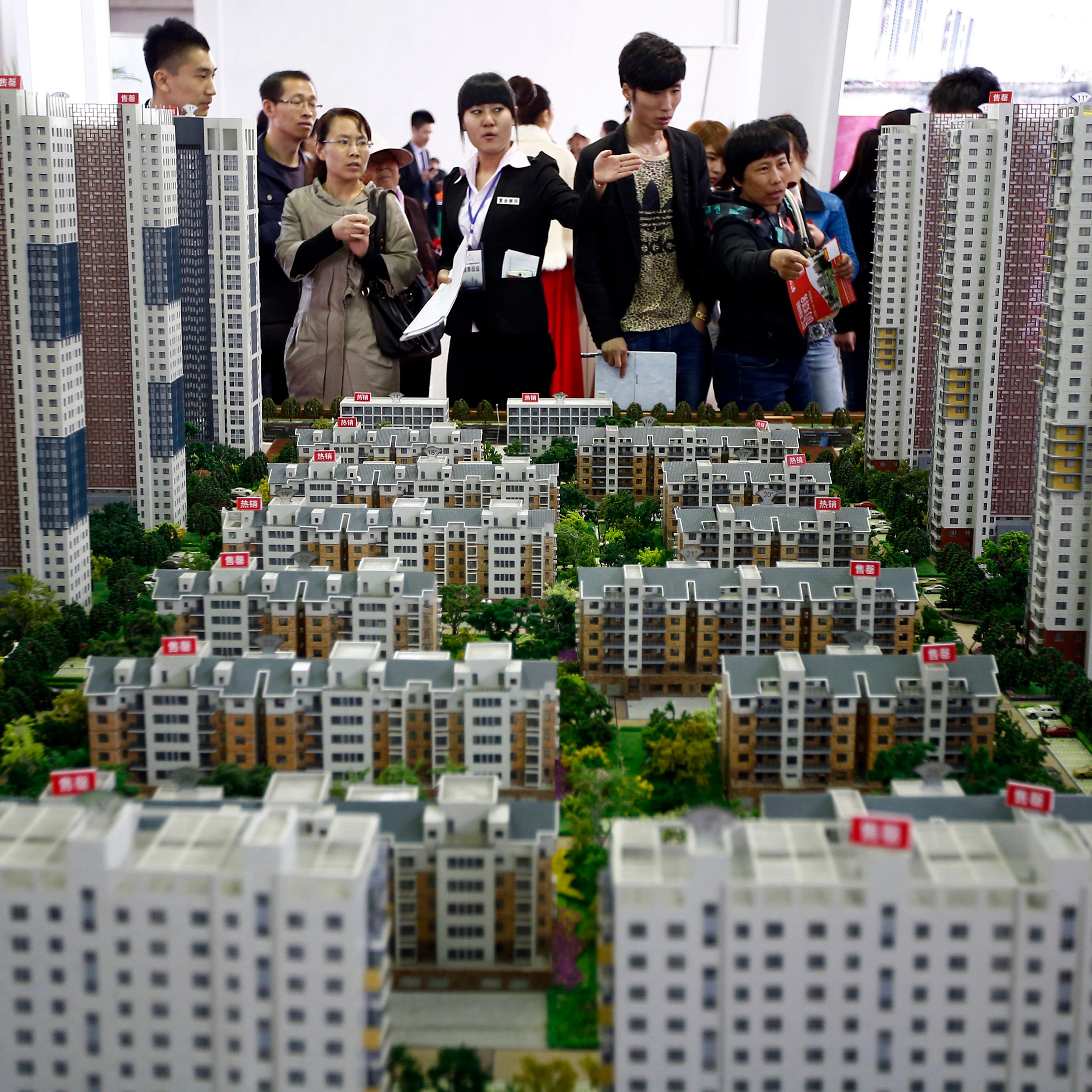 A sales assistant talks to visitors in front of models of apartments at a real estate exhibition in Shenyang