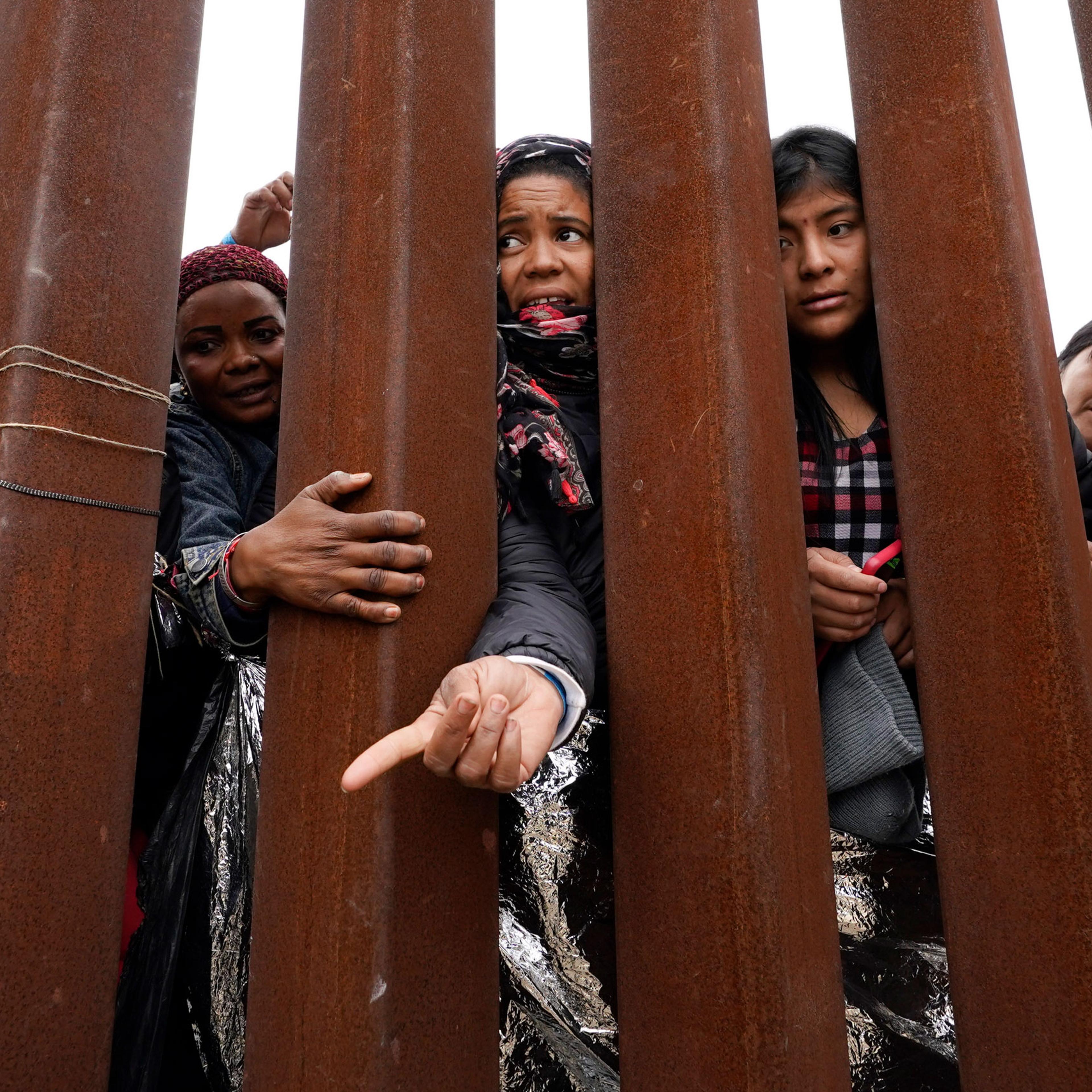 Migrants reach through a border wall for clothing handed out by volunteers, as they wait between two border walls to apply for asylum in San Diego