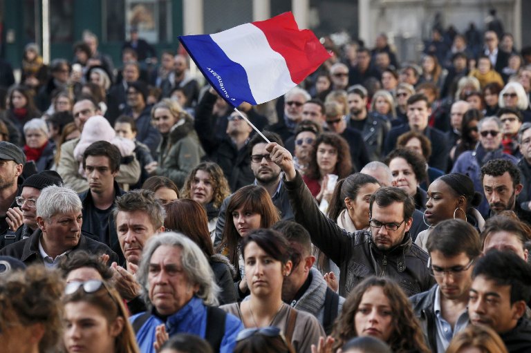 A man waves a French flag as several hundred people gather to observe a minute of silence in Lyon, to pay tribute to the victims of the series of deadly attacks in Paris