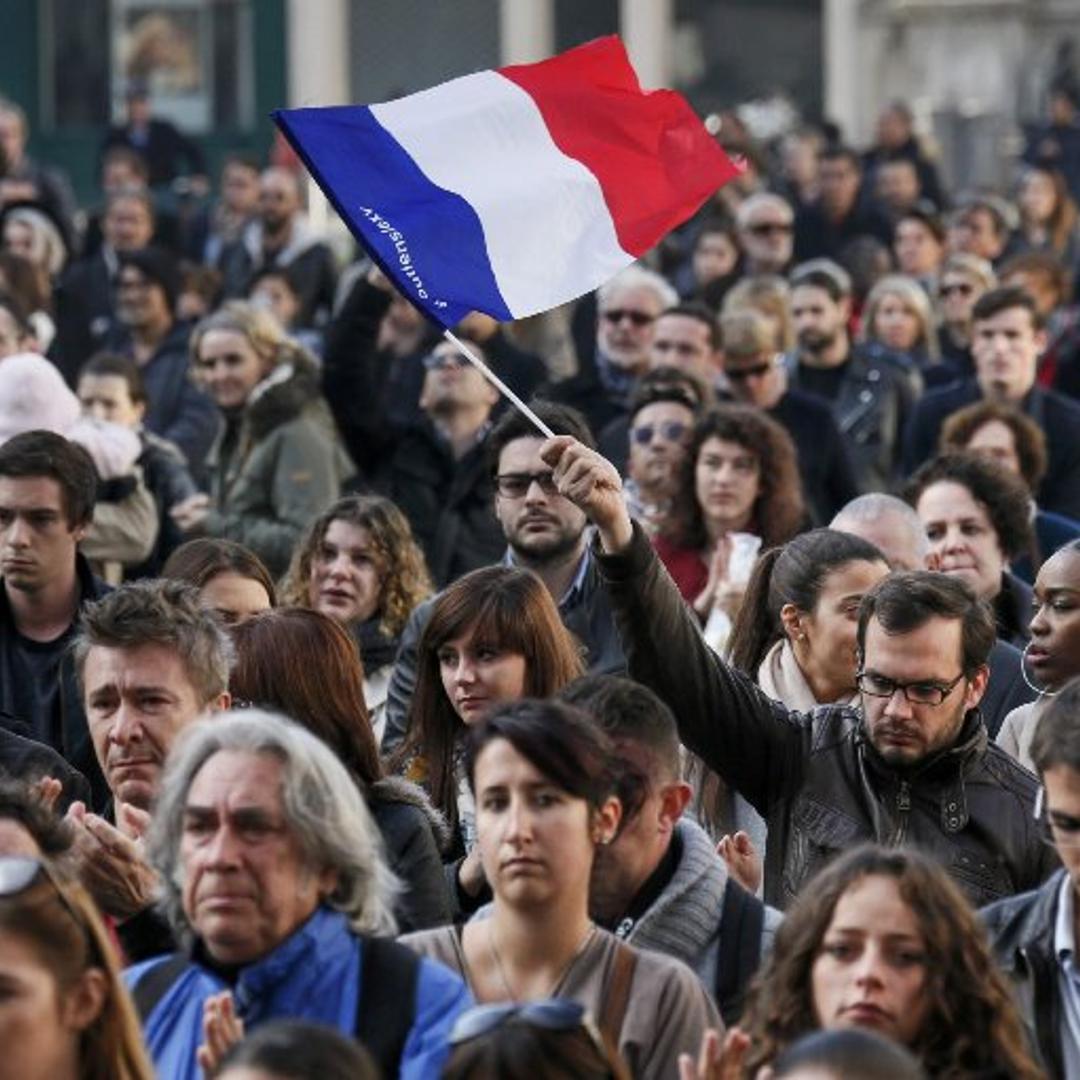 A man waves a French flag as several hundred people gather to observe a minute of silence in Lyon, to pay tribute to the victims of the series of deadly attacks in Paris
