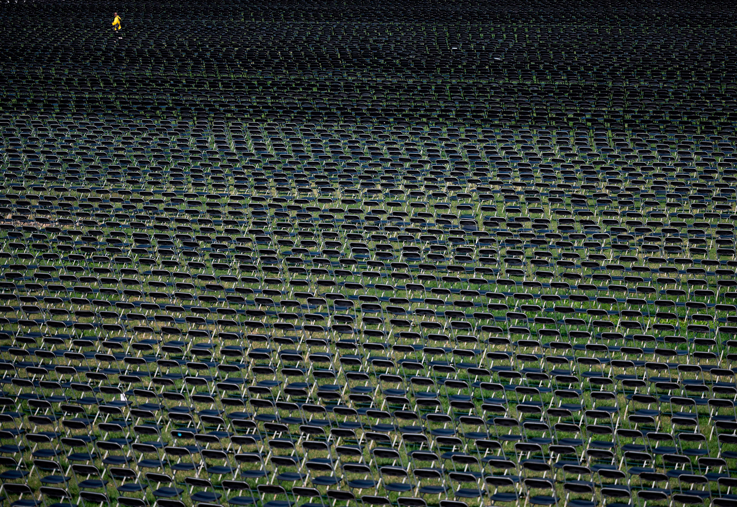 An event staff member walks past the empty chairs on display to represent the 200,000 lives lost due to COVID-19 on the ellipse behind the White House on Oct. 4
