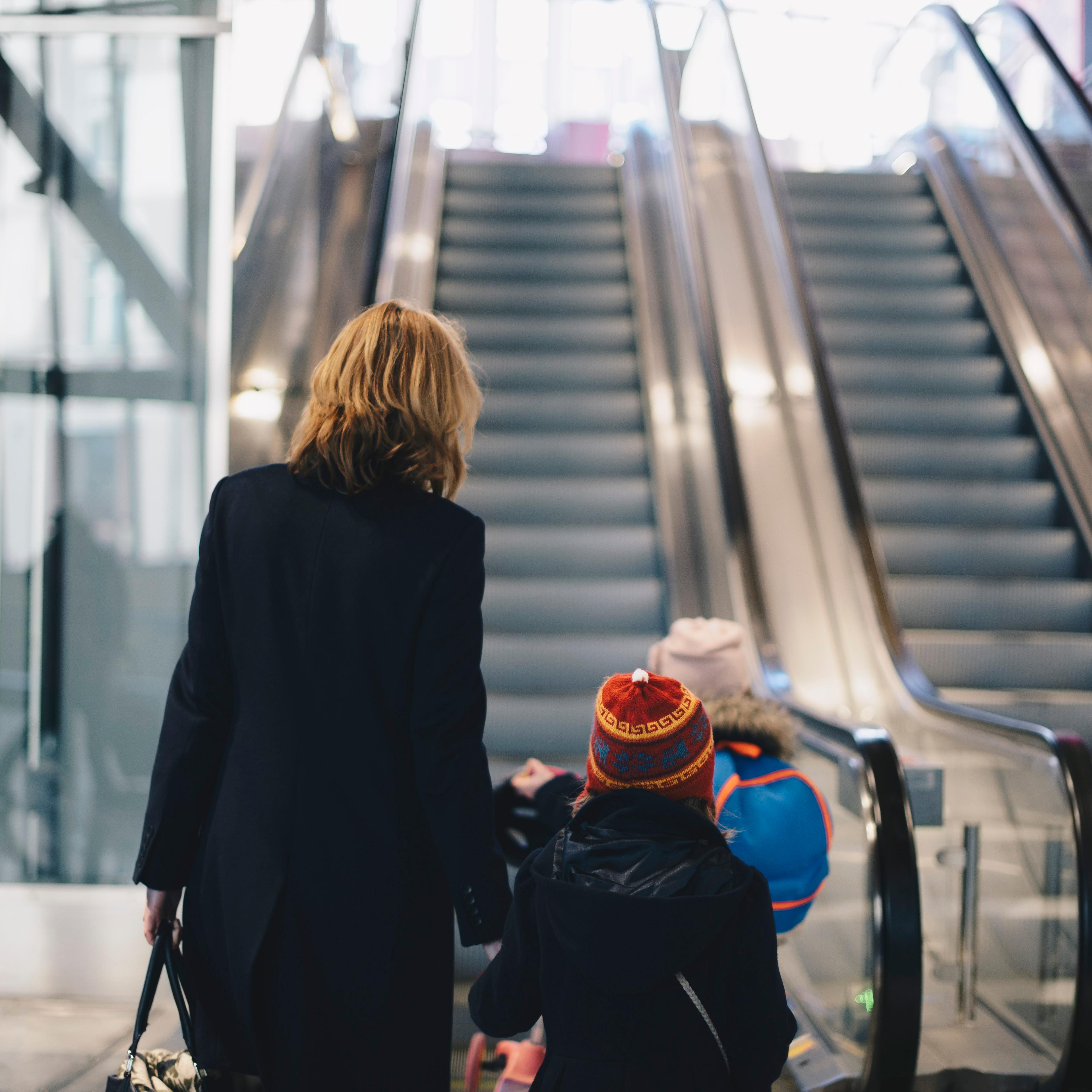 Rear view of mother and daughters walking towards escalator at railroad station