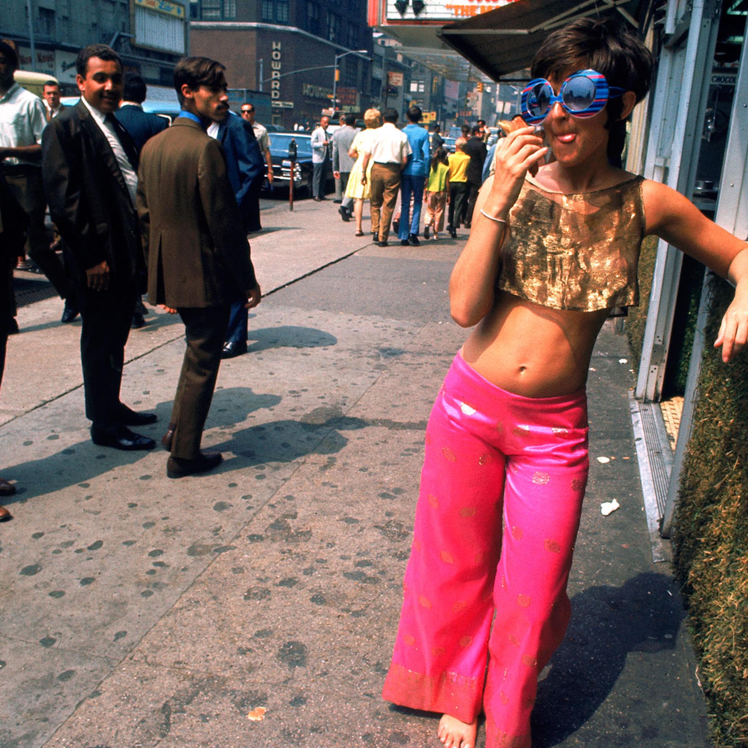 Men ogle a young woman wearing pink pants and a gold top, New York City, summer 1969.