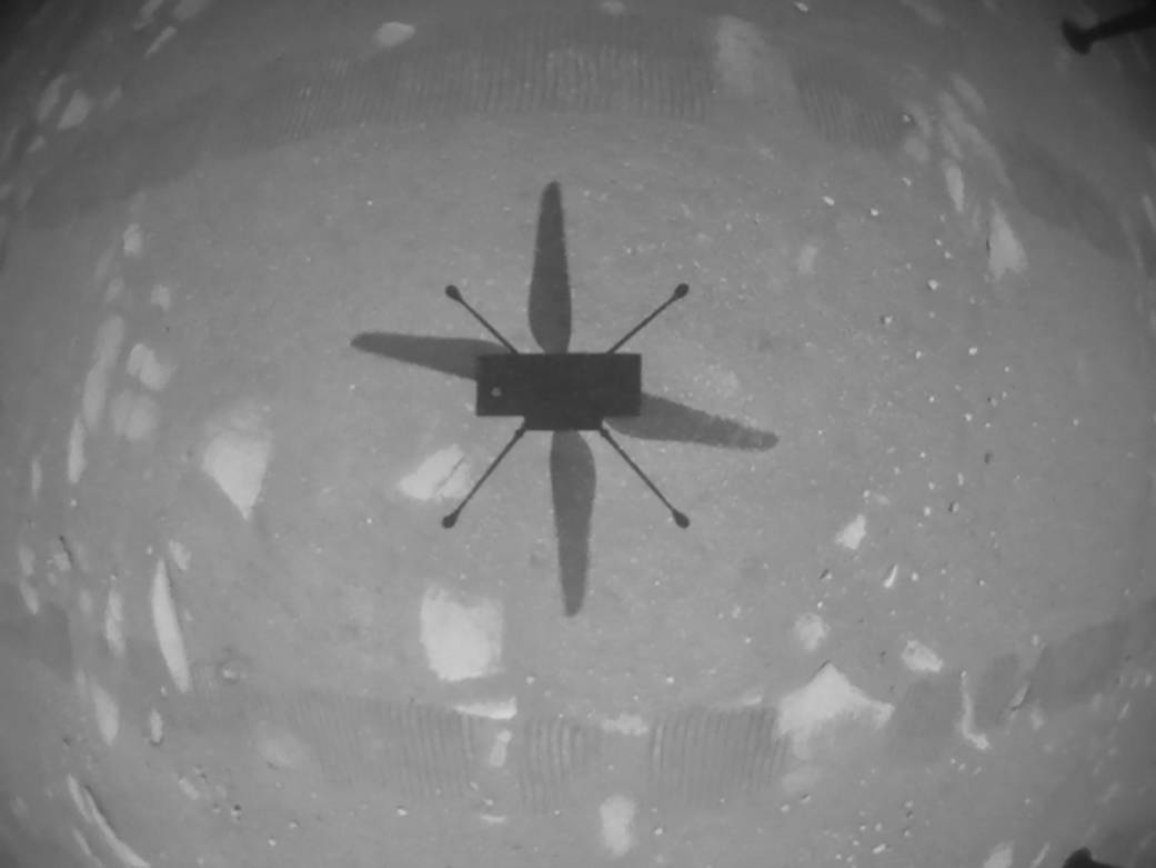 A downward facing camera aboard the Ingenuity helicopter captures the vehicle's shadow as it hovers about 3 meters off the ground.