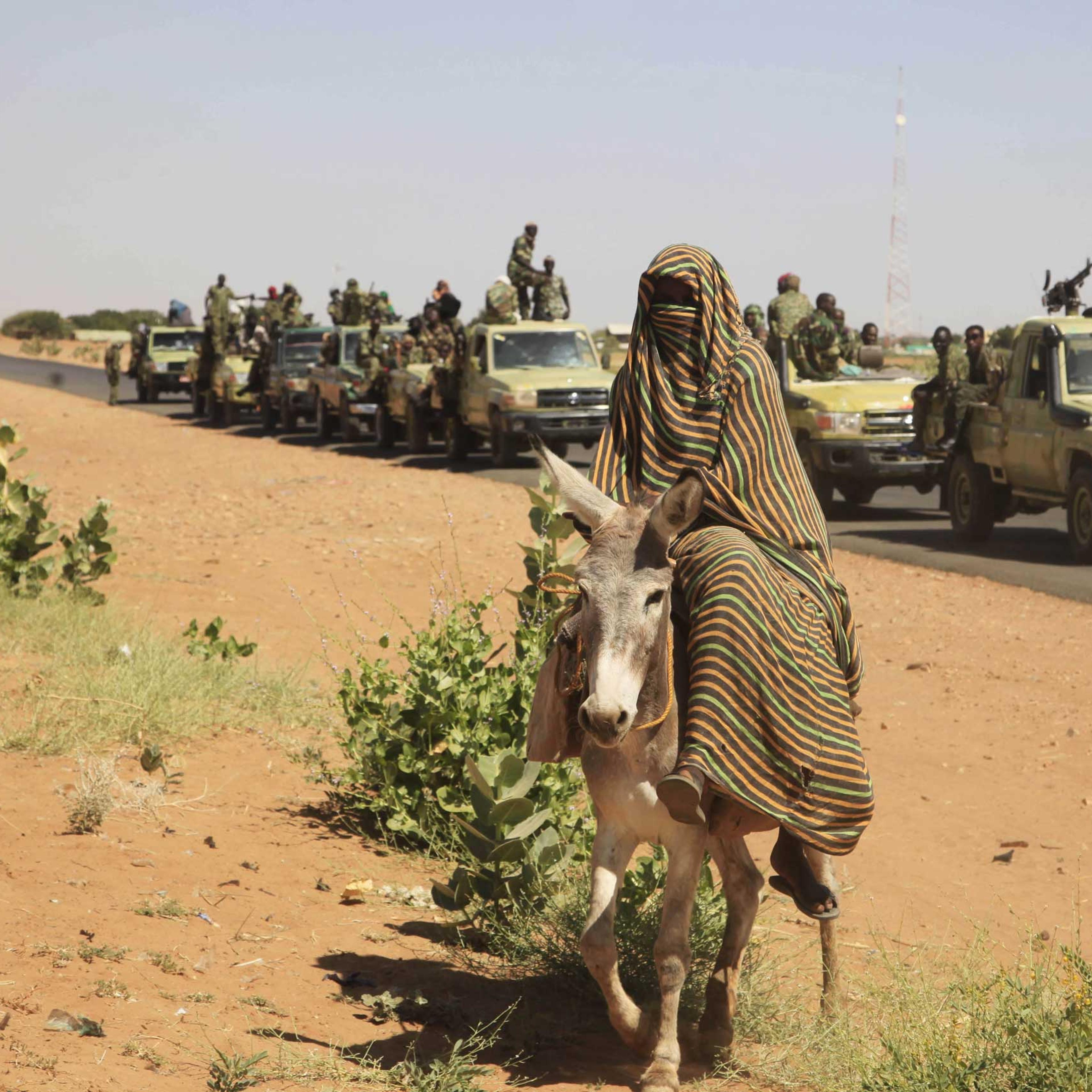 A woman rides a donkey past a convoy of government troops in Tabit village in the North Darfur region of Sudan, Nov, 2014.