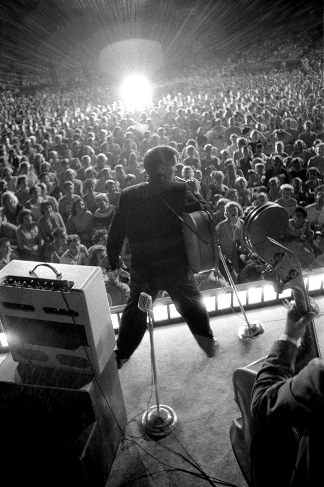 July 4, 1956. Russwood Park, Memphis. This is one of my iconic shots, which is called “starburst.” I’m above the stage and have my frame set. This young lady, maybe a hundred feet back from stage, let’s go with a flash and it backlights everything I’ve got.  It separates the foreground, makes it into a silhouette, and it “flares” me… this is part of my internal camera/shutter apparatus, and makes this entire picture. Without it, it was a dull picture.  He told the audience, "Tonight you will see the real Elvis Presley," then proceeded to gyrate all over the stage to the delight of the 14,000 crowd.