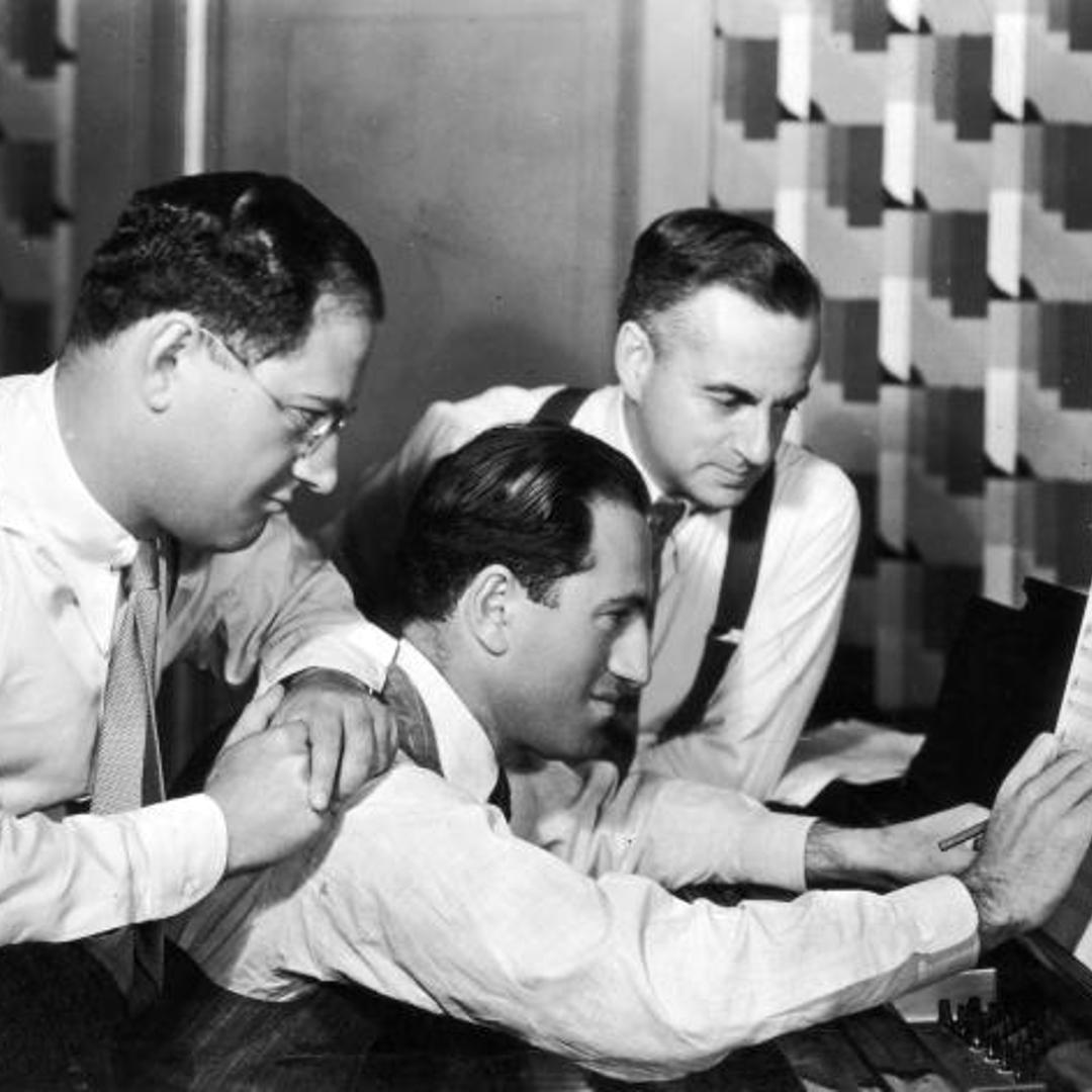 Circa 1925: George Gershwin (1888 - 1937) (C) at work as his brother and songwriting partner, lyricist Ira Gershwin (1896 -1983) (L), and British dramatist Guy Bolton (1884 - 1979), look on.