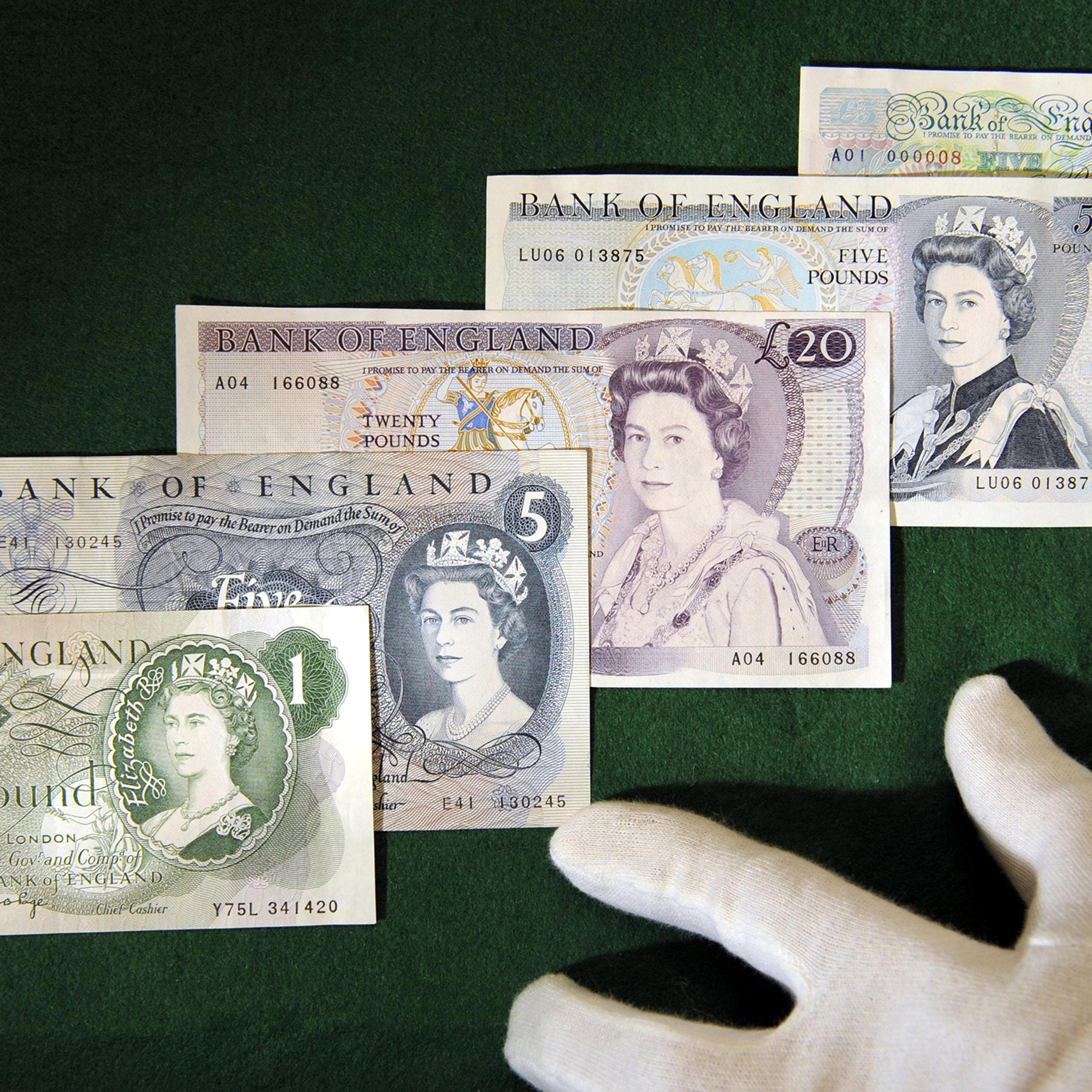 A curator displays a series of banknotes featuring Queen Elizabeth II. They are (top to bottom) a £5 note from 1990, a £5 note from 1971, a £20 note from 1970, a £5 note from 1963 and the first £1 note - from 1960 - at the Bank of England Museum in London, March 2010.